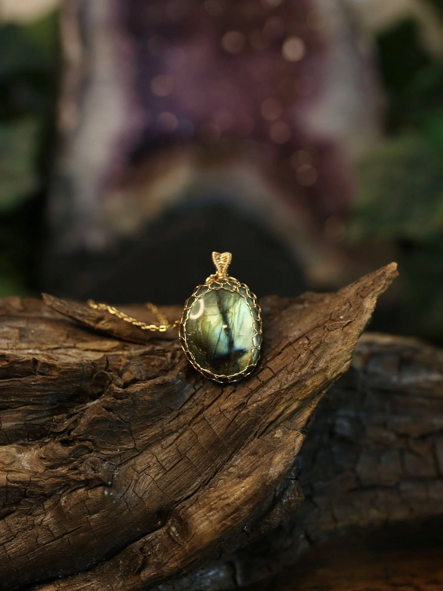 A necklace with a large rectangular labradorite gemstone displaying an iridescent purple and blue flash, set in a gold band, placed on a small red dish.