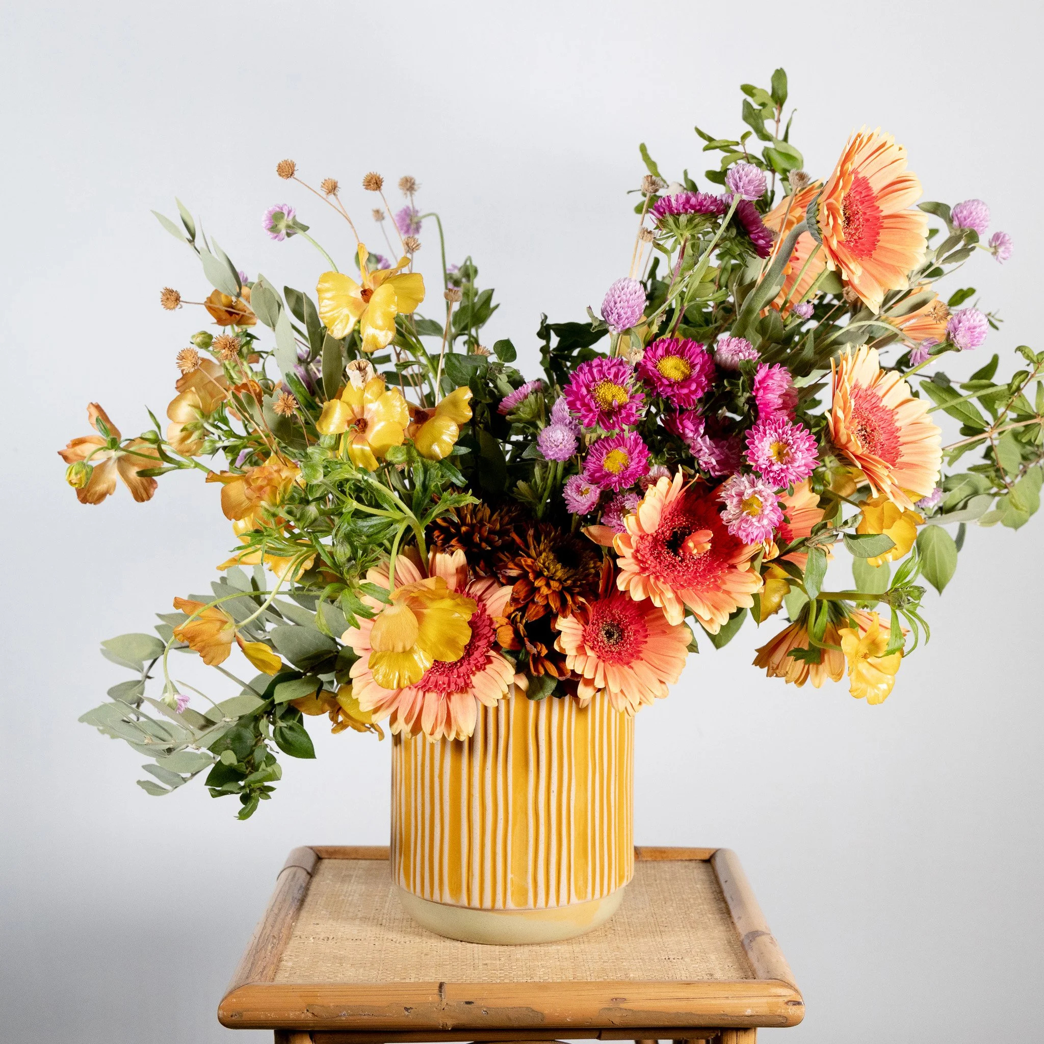 A colorful bouquet of mixed flowers in a yellow striped vase on a wooden table.