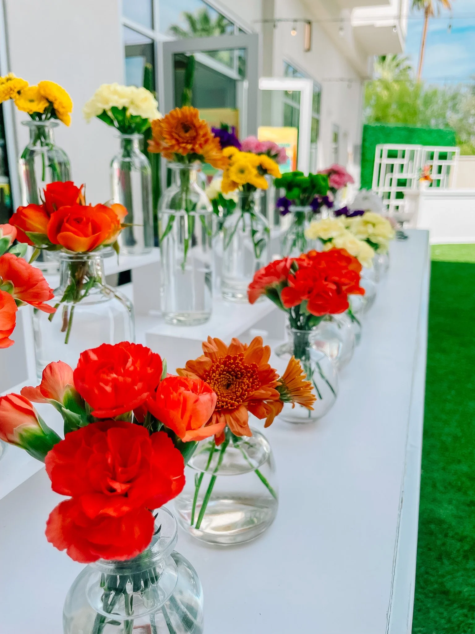 Bud vases filled with flower stems arranged by the colors of the rainbow. The bud vases are on a white bar top.