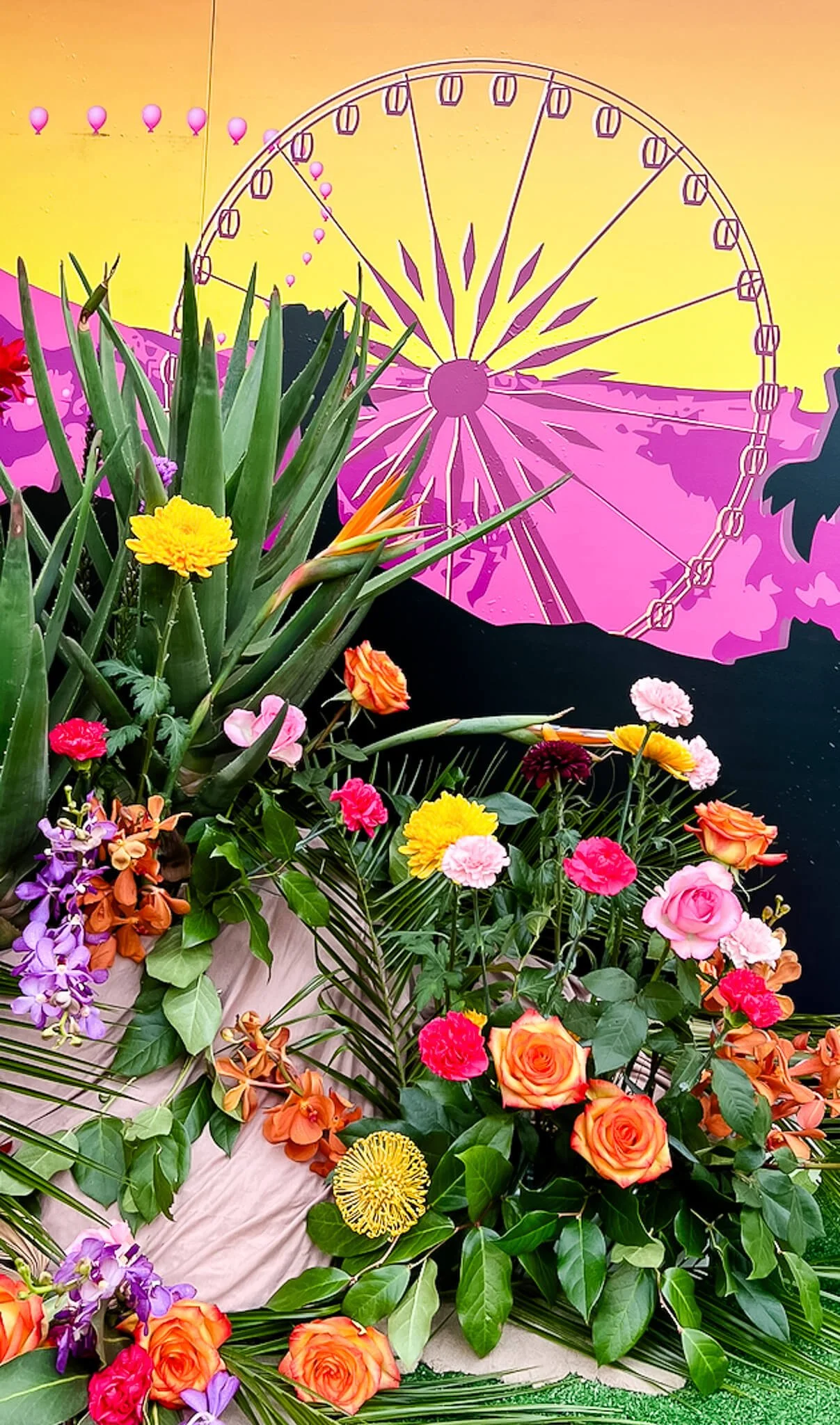 Close-up of a floral ground installation for an event, showcasing desert plants, dried textures, and sand dunes arranged in front of a branded festival neon light display