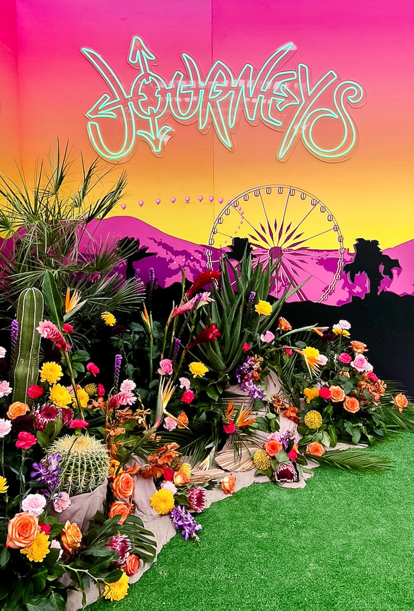 Side-angle view of a desert-inspired floral installation at a brand activation, highlighting the depth of the floral layers and sand dunes against a neon-lit festival photo backdrop."