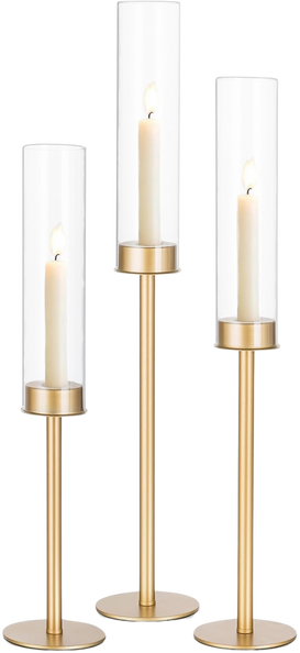 Three decorative candle holders with candles and glass hurricanes, featuring gold accents and white candles of varying heights.