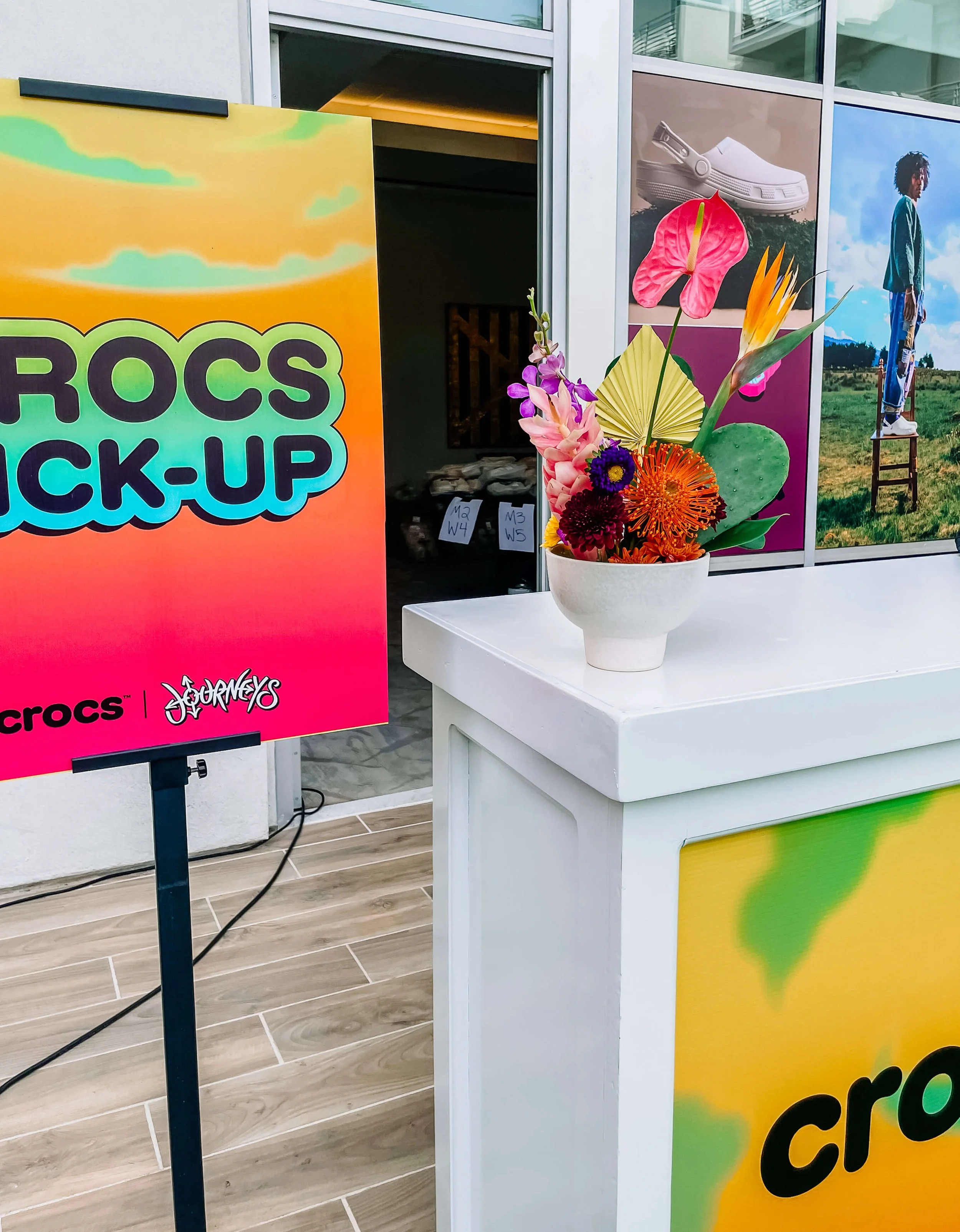 A bright colorful arrangement sits on top of a bar. Event brand signs for Crocs and Journeys are next to it and below it.