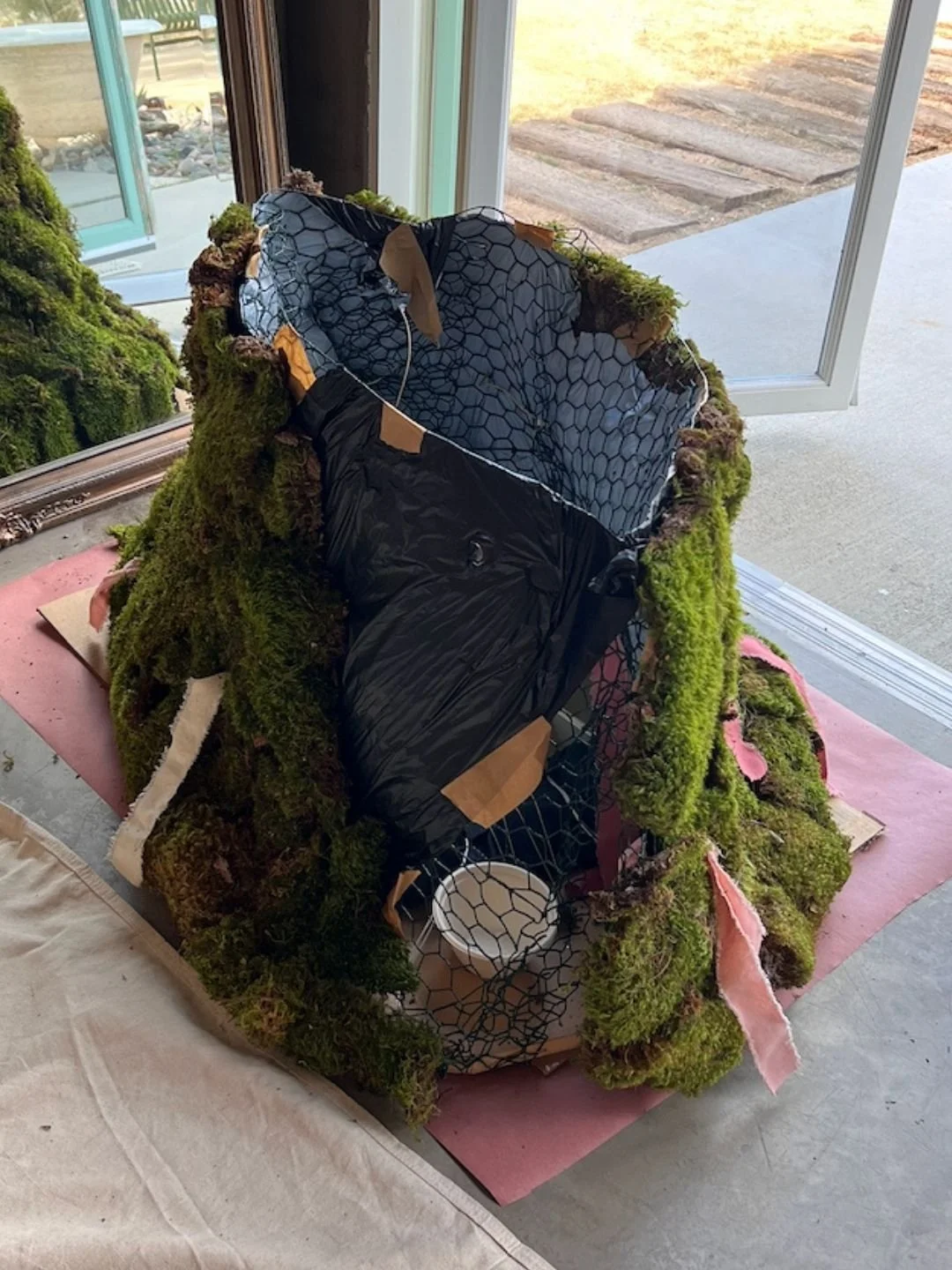 The base of the arch under construction showing layers of moss, black film, chicken wire, MDF board, and plant fiber cups.