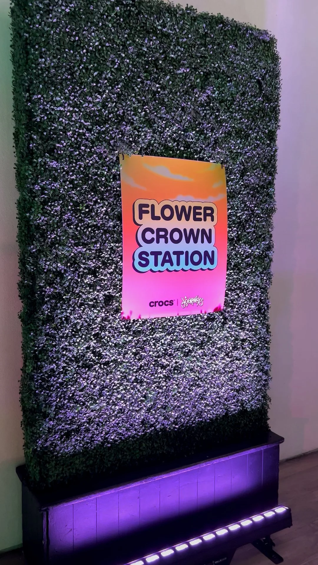 Green hedge against a wall with a poster attached that reads Flower Crown Station and the Crocs and Journeys logos.