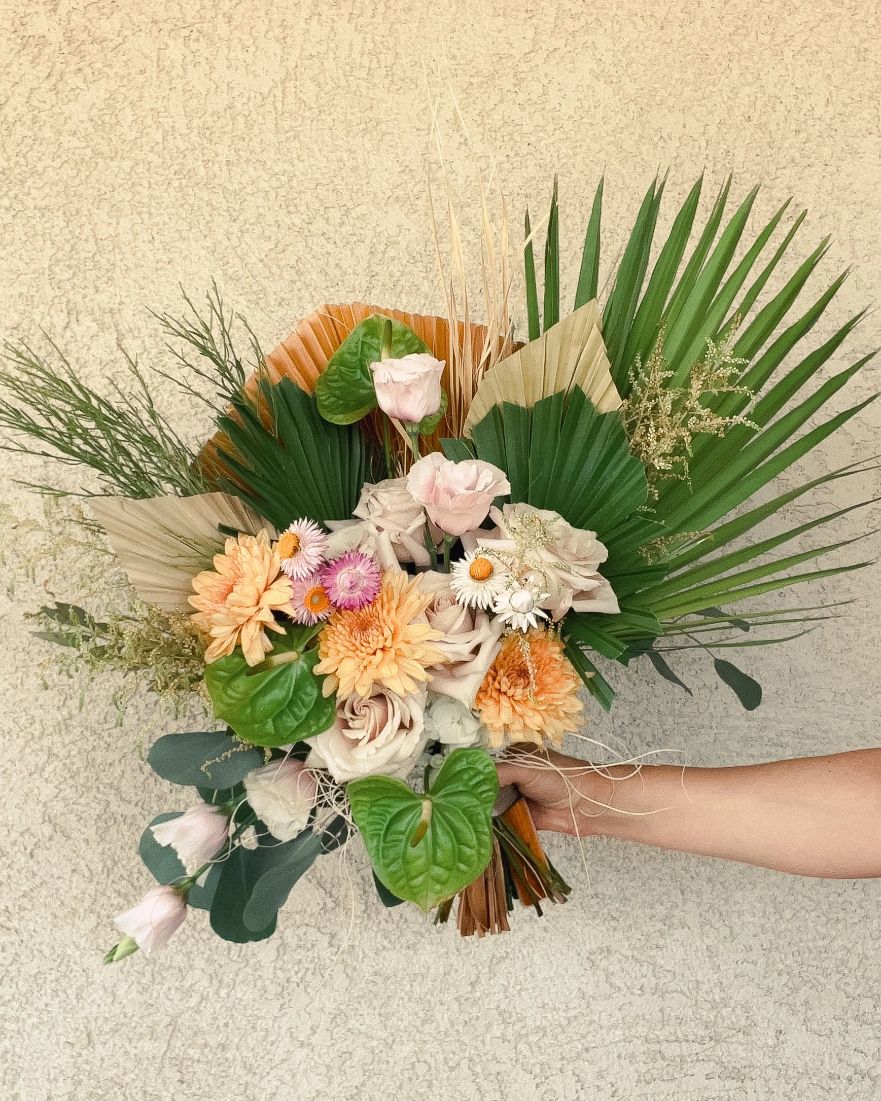 A bridal bouquet with green anthurium, dried and fresh palm fronds, lisianthus, jojoba leaves, Mojave yucca fibers, astilbe, roses, mums, desert broom, and strawflowers.