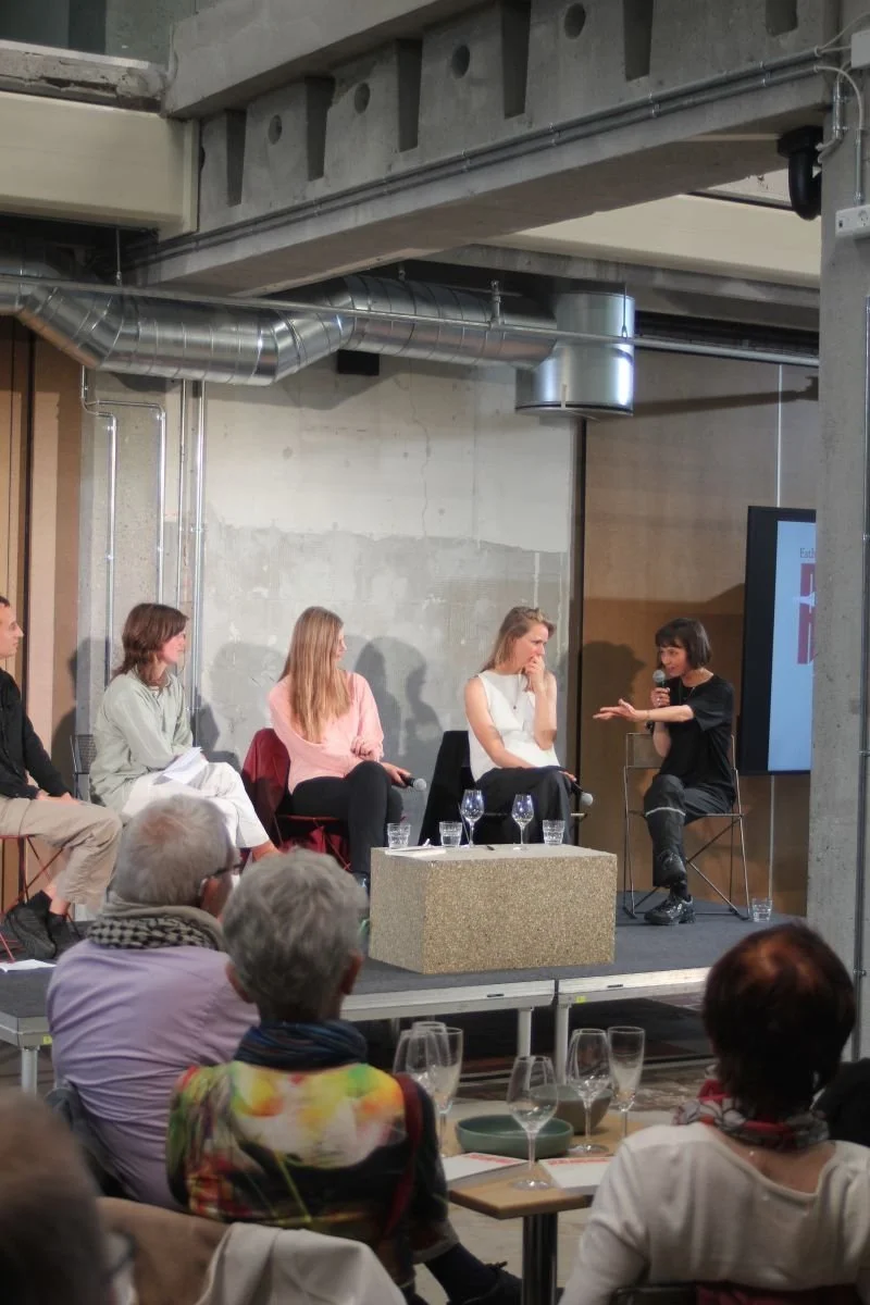 En paneldeltager diskuterer med publikum under en samtalepanel i en industriel indretning.