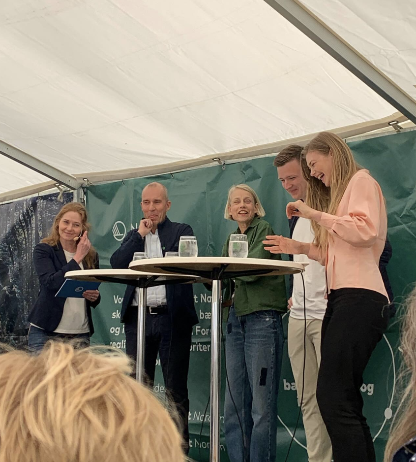 Fem personer, herunder Tanja Gotthardsen, den tidligere Forbrugerombudsmand og direktøren for Miljømærkning Danmark, står på en scene hos Nordisk Ministerråd under en telt, ler og har samtale.