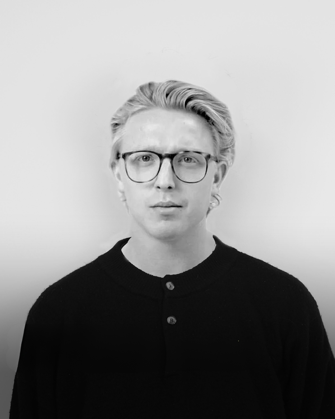 Sort-hvid portræt af Kasper Bjørkskov med lyst, stylet hår, briller og sort sweater mod en lys baggrund.