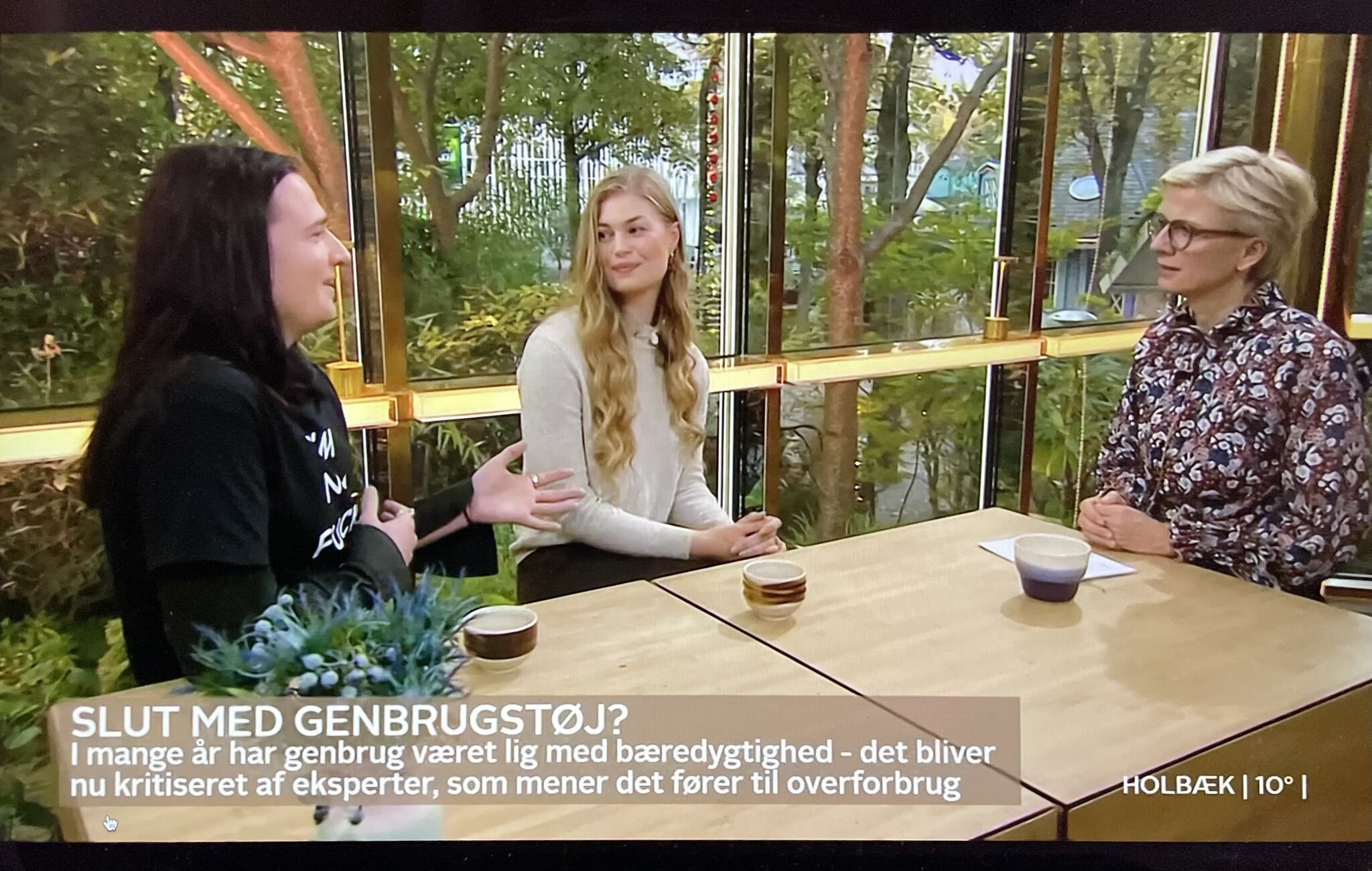 Tanja Gotthardsen i Go' Morgen Danmark på TV2, sammen med en anden gæst. Bag dem ses store vinduer, der vender ud mod en grøn have med træer og buske.