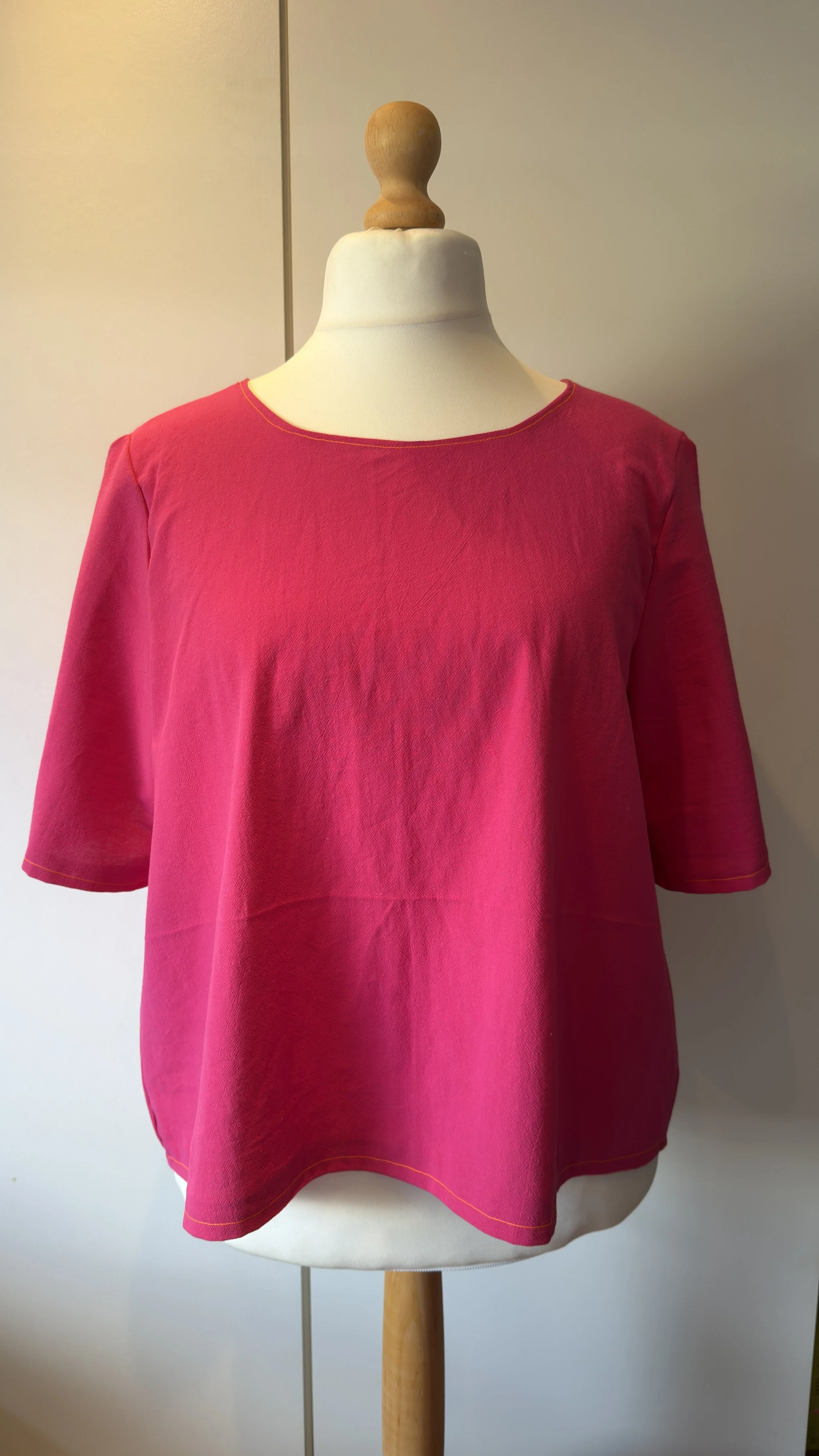 A mannequin wearing a bright pink T-shirt with yellow stitching, set against a light background.