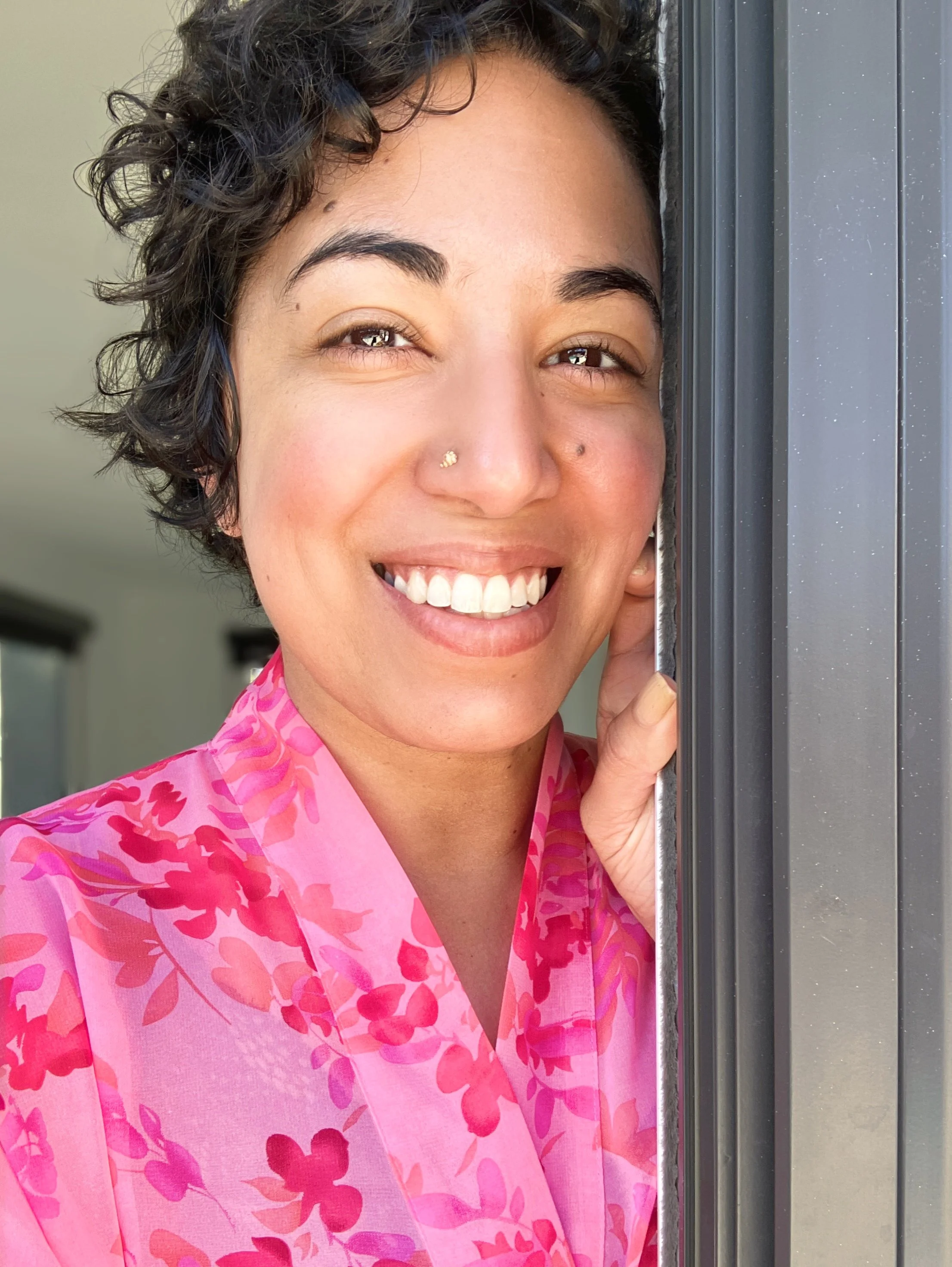 Image of a smiling, sunlit brown-skinned woman with short, curly black hair.