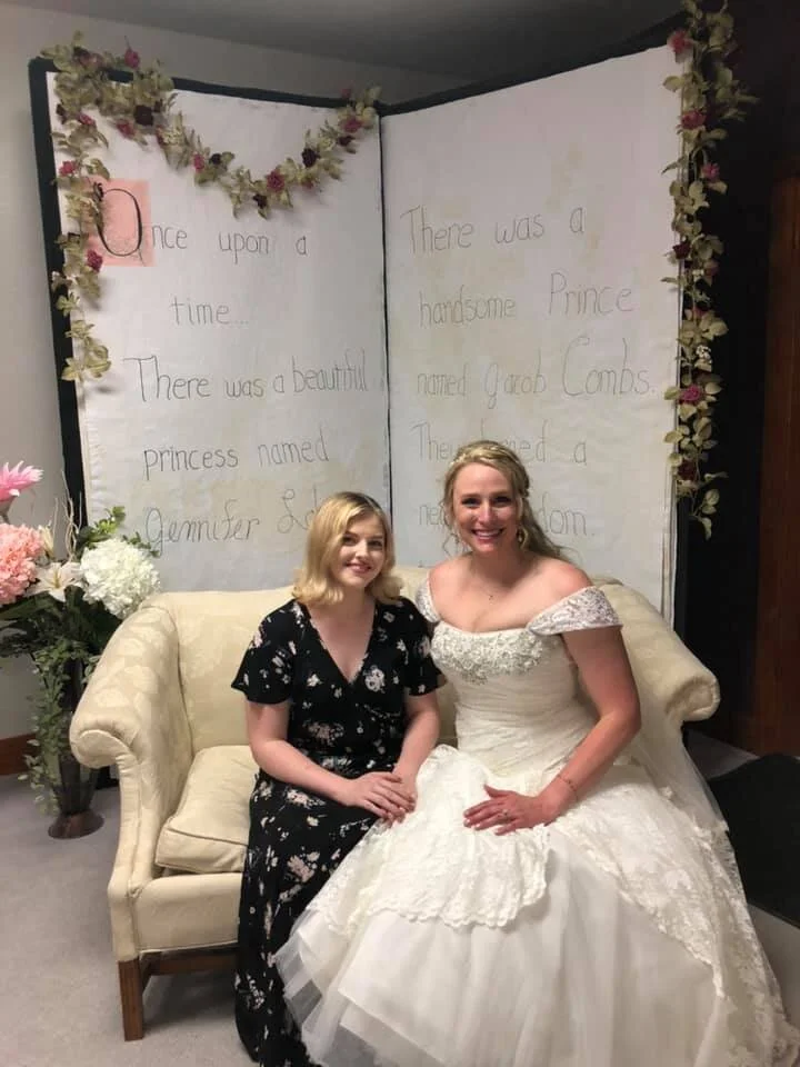 Bride and friend sitting in front of giant fairy tail book at Life's Finer Moments Kansas wedding venue
