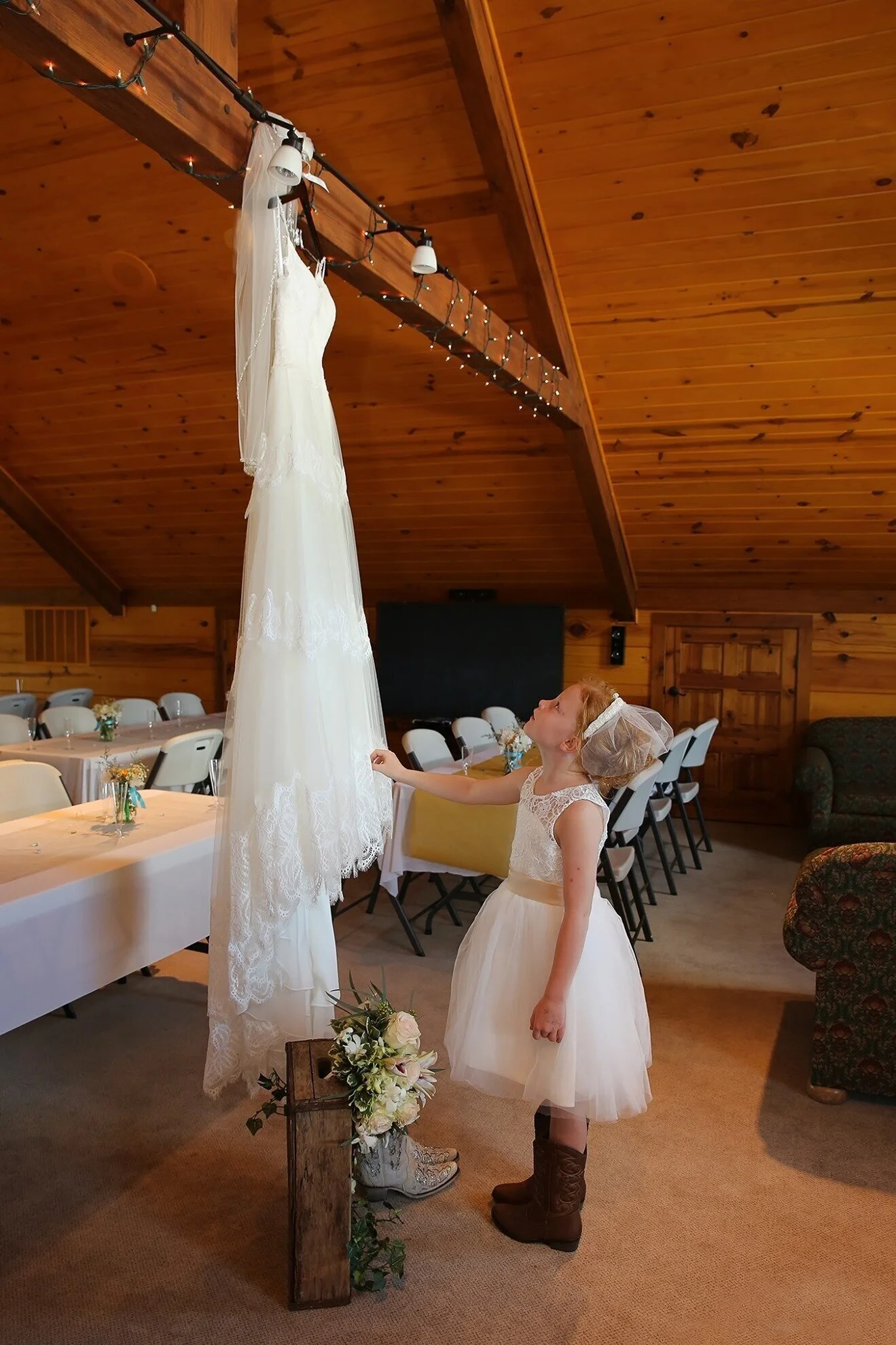 Small girl looking at bride's gown hanging from beam in Life's Finer Moments venue.