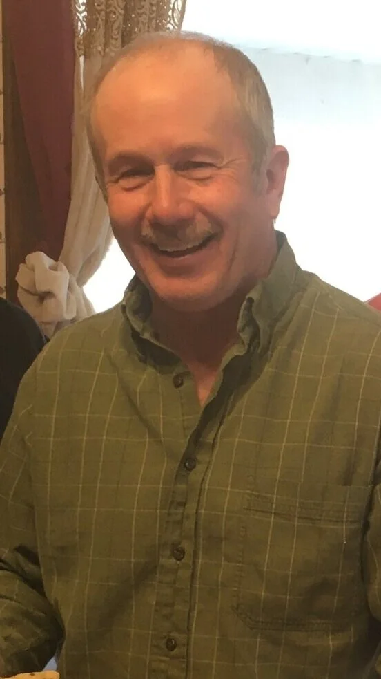 Smiling middle-aged man with short gray hair wearing a green plaid shirt.