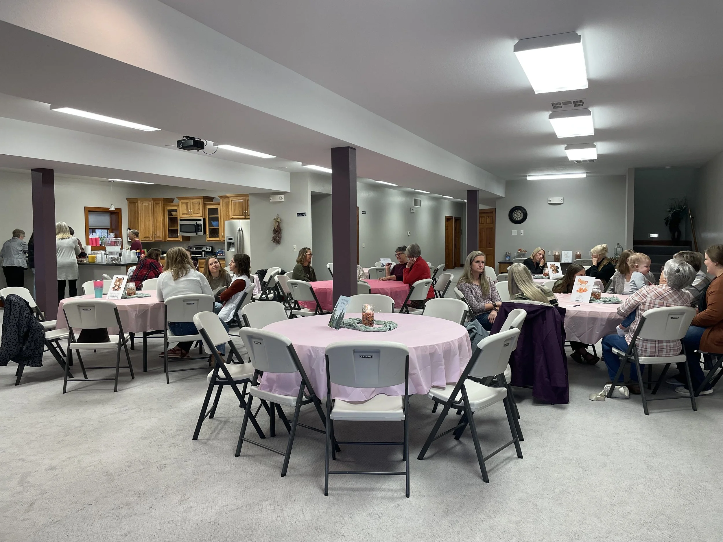 Decorated round tables for baby shower in carpeted room with kitchen