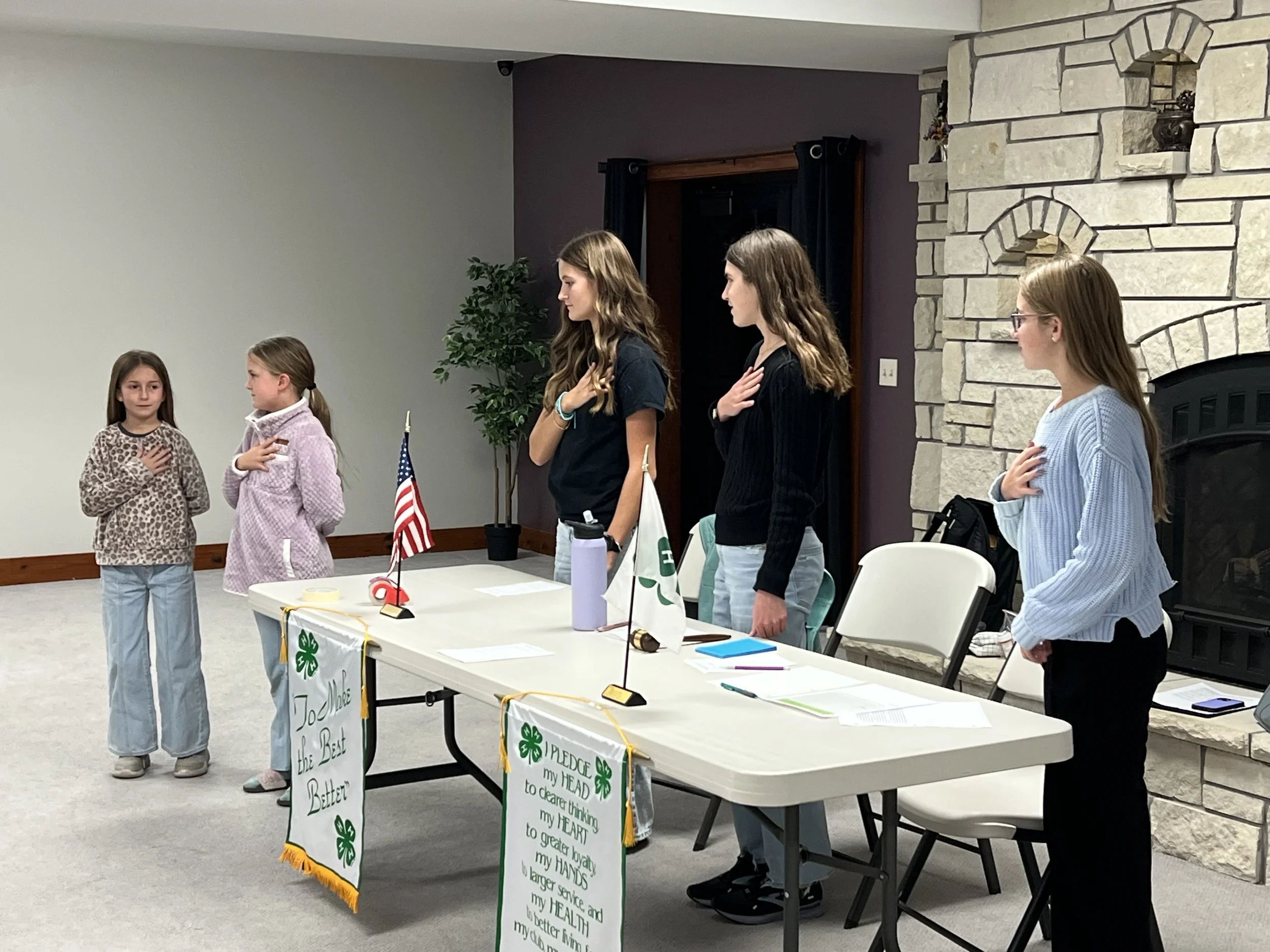 4H group meeting with flags and members standing with hands on hearts at Clay Center venue.