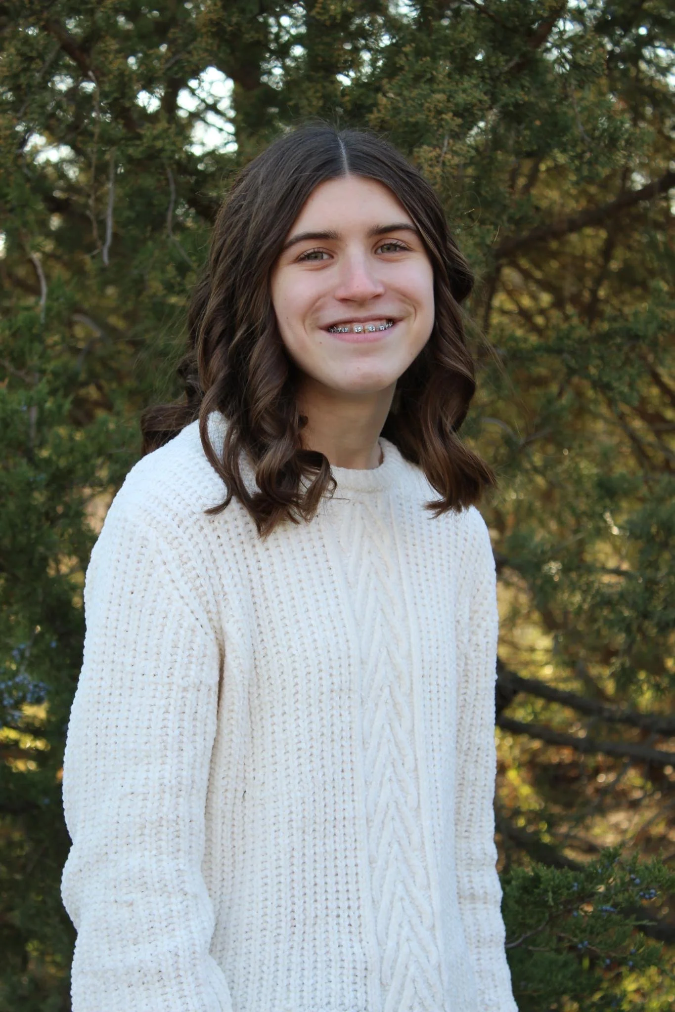 Girl standing in front of evergreen in white sweater