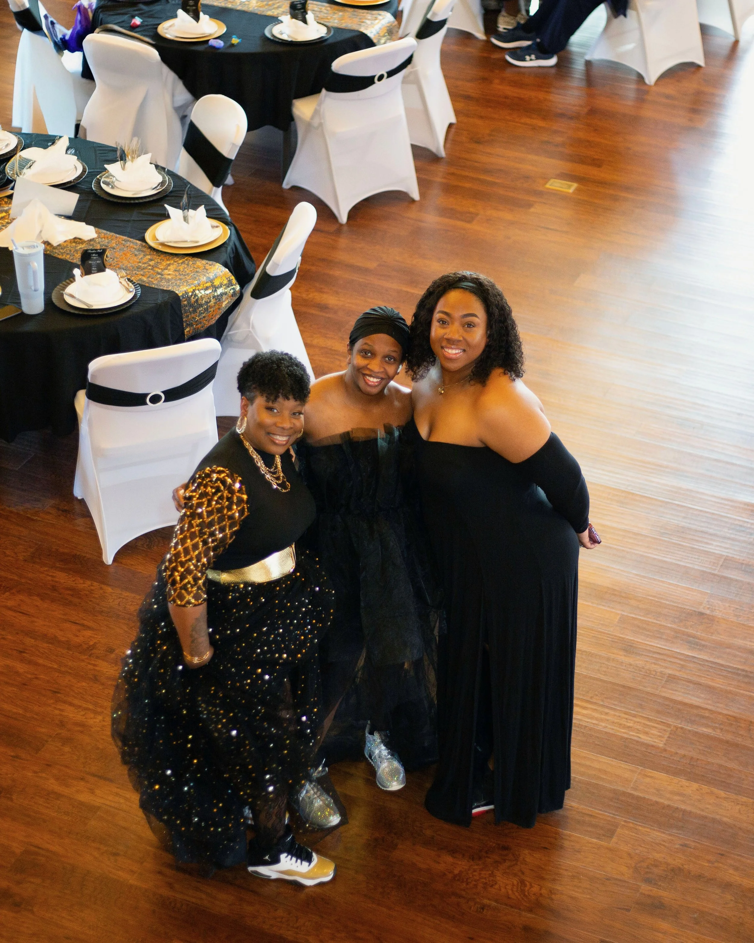 Women in formal gowns and tennis shoes at banquet in large wood room at venue in Clay Center.