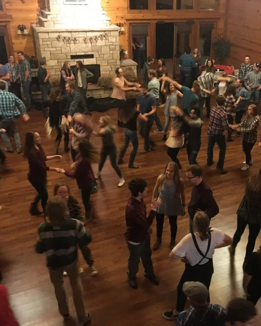 Hundreds of college agers swing dancing in large log cabin with fireplace