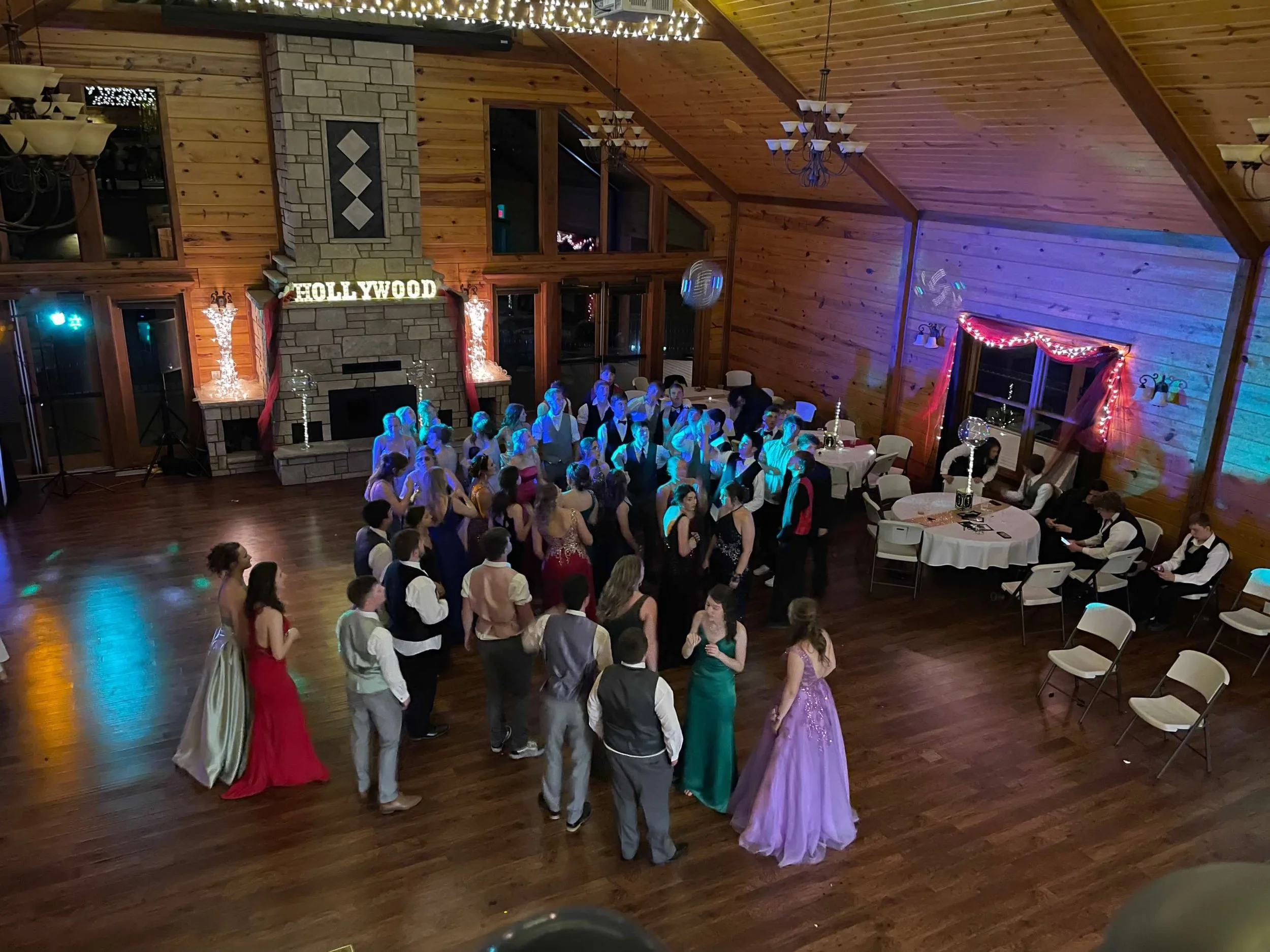 Prom dancers with Hollywood decorations in large log room with chandeliers and tall fireplace.