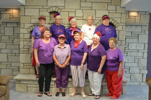 Red Hat Society ladies in purple clothes in front of limestone fireplace