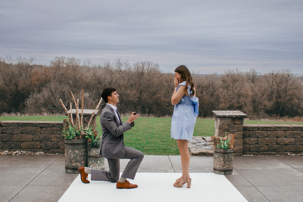 Wedding proposal on knee with ring to girl in blue on patio of Life's Finer Moments