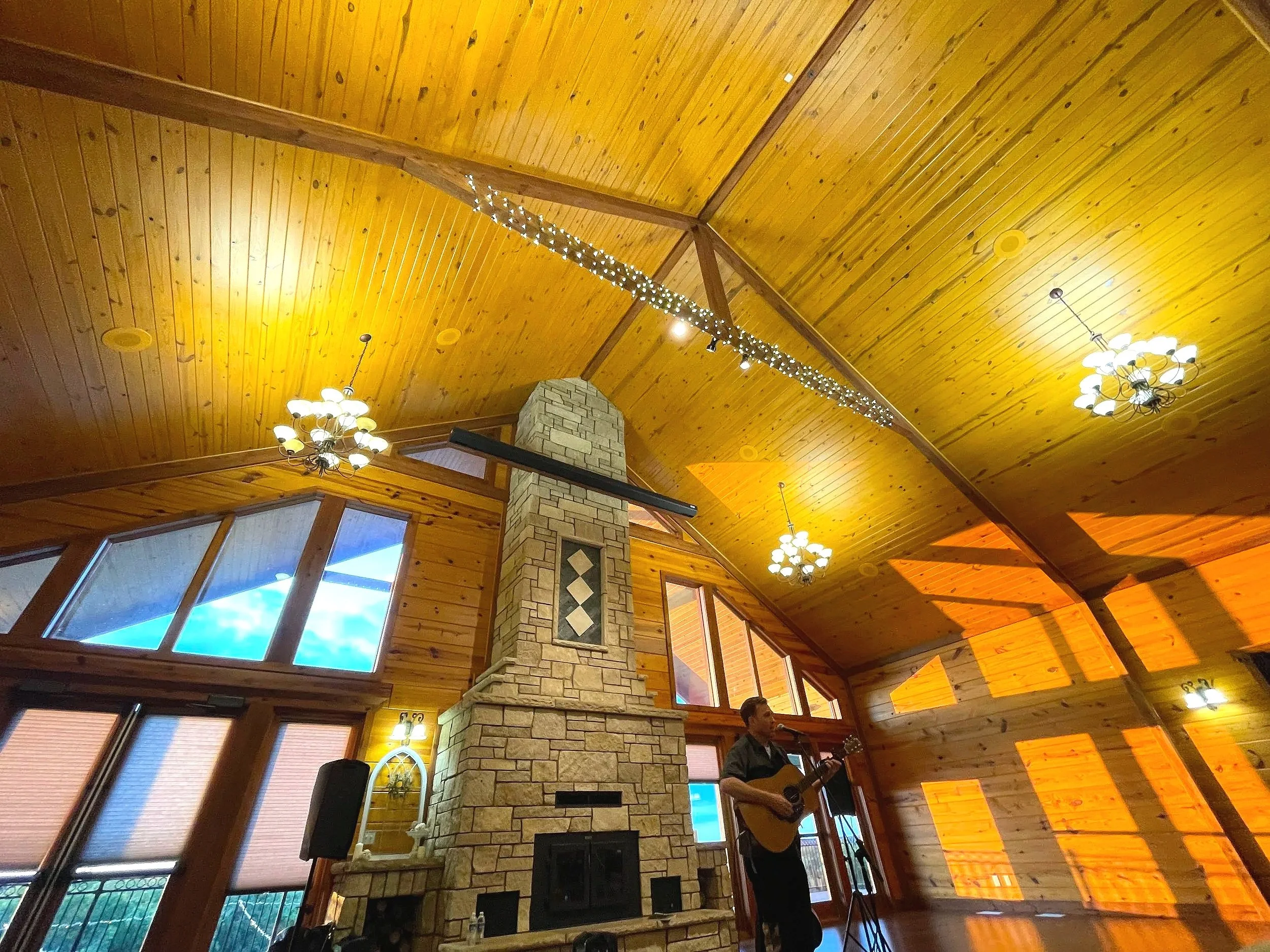 Guitarist playing at sunset in front of tall windows in log room with chandeliers and fireplace