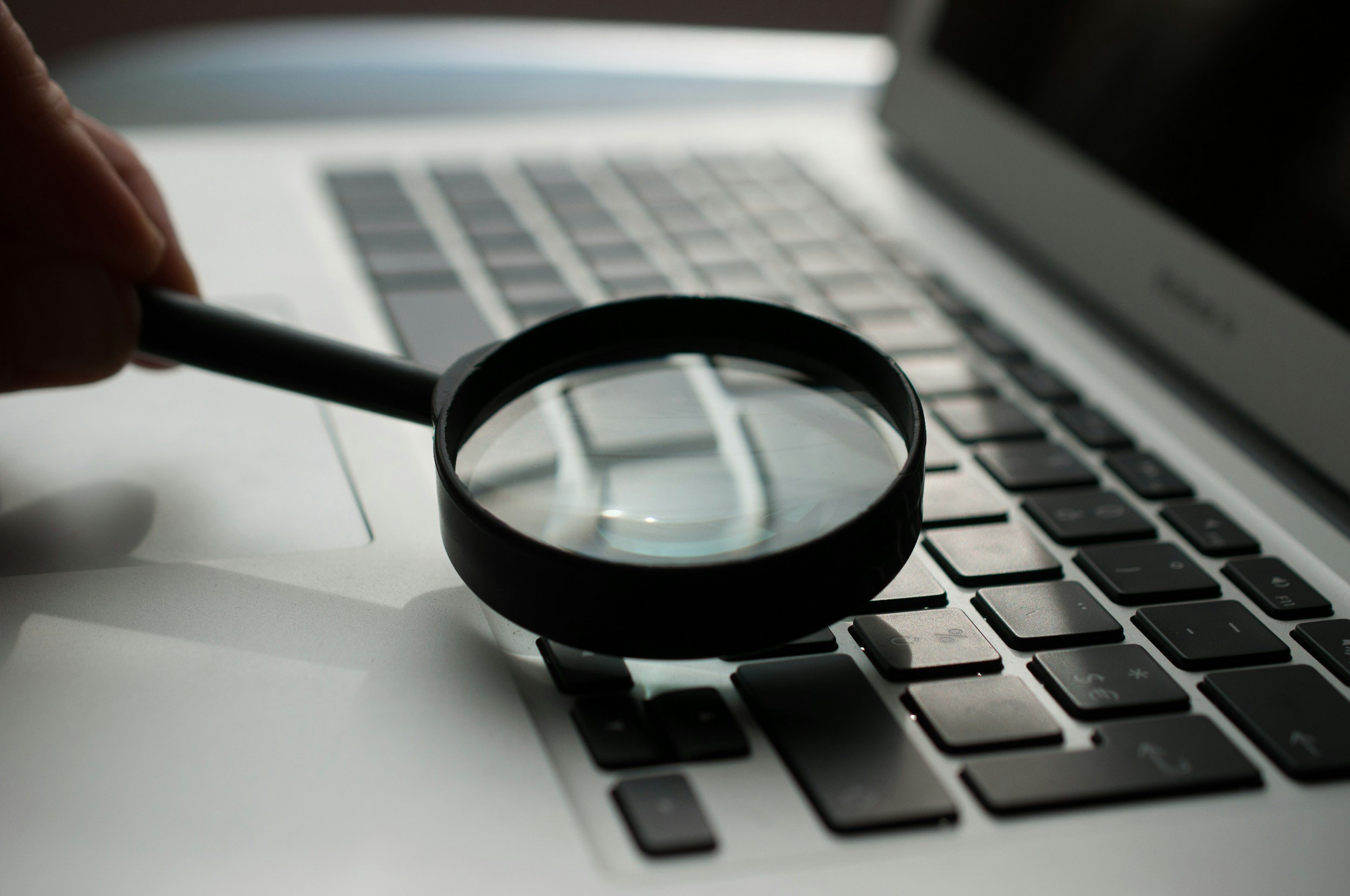 A magnifying glass held by a person's hand over a laptop keyboard.