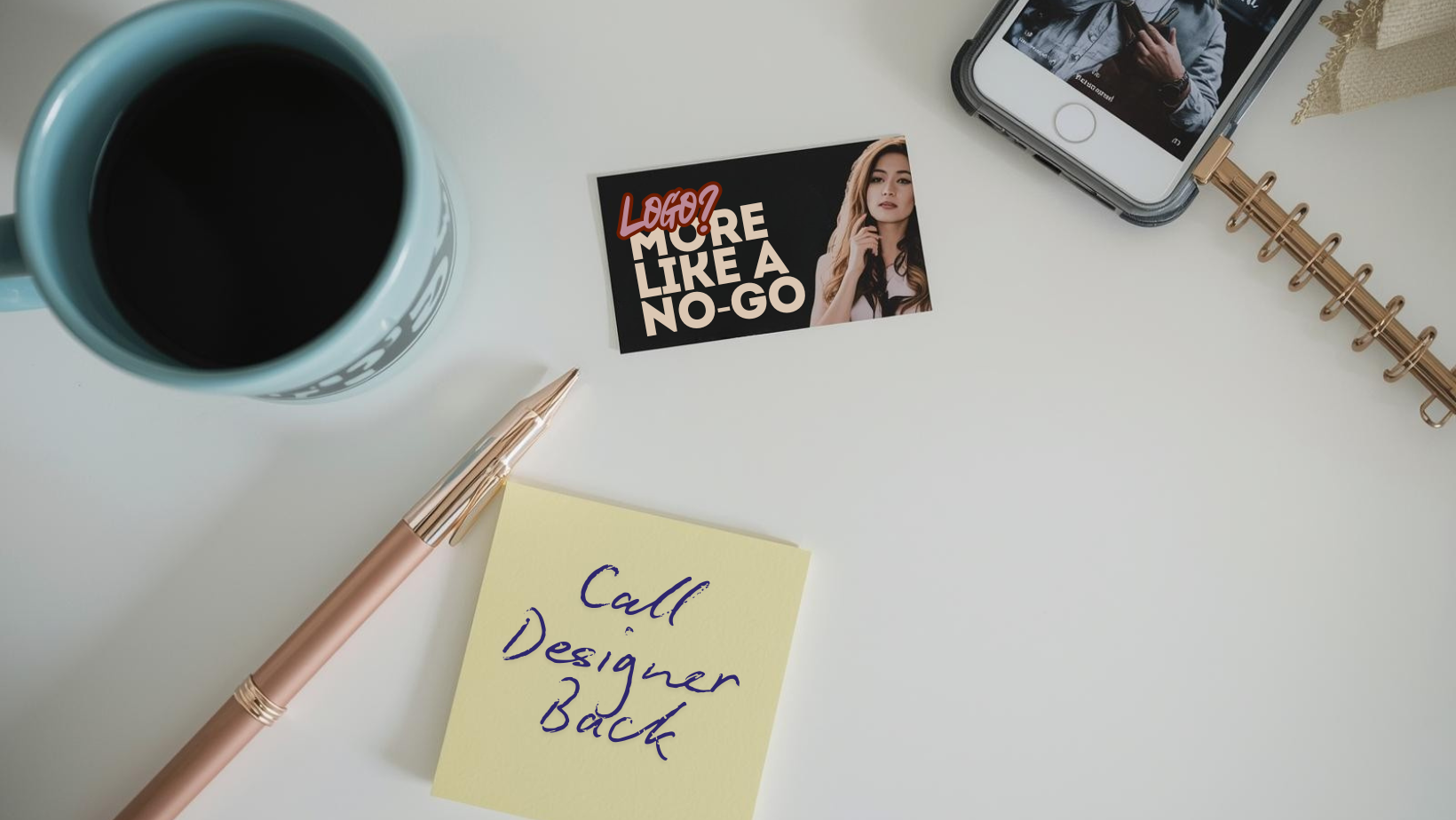 Cluttered desk with phone, coffee mug, rose gold pen and spiral notepad, with business card and post it note that says Call Designer Back