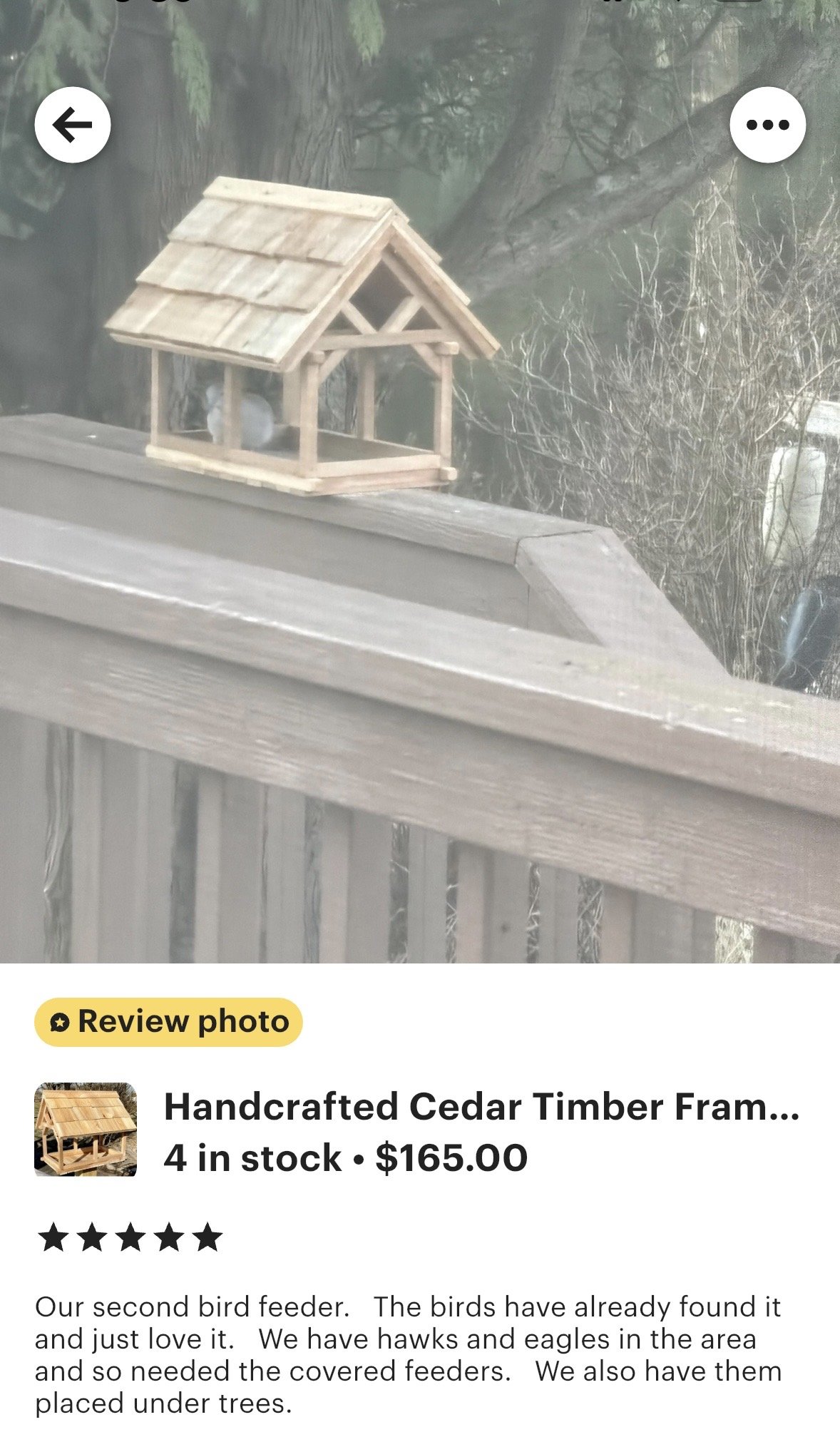 Timber Frame style Bird Feeder with shake shingled roof, all made from Cedar,  mounted on a wooden railing outdoors. Bird is eating.
