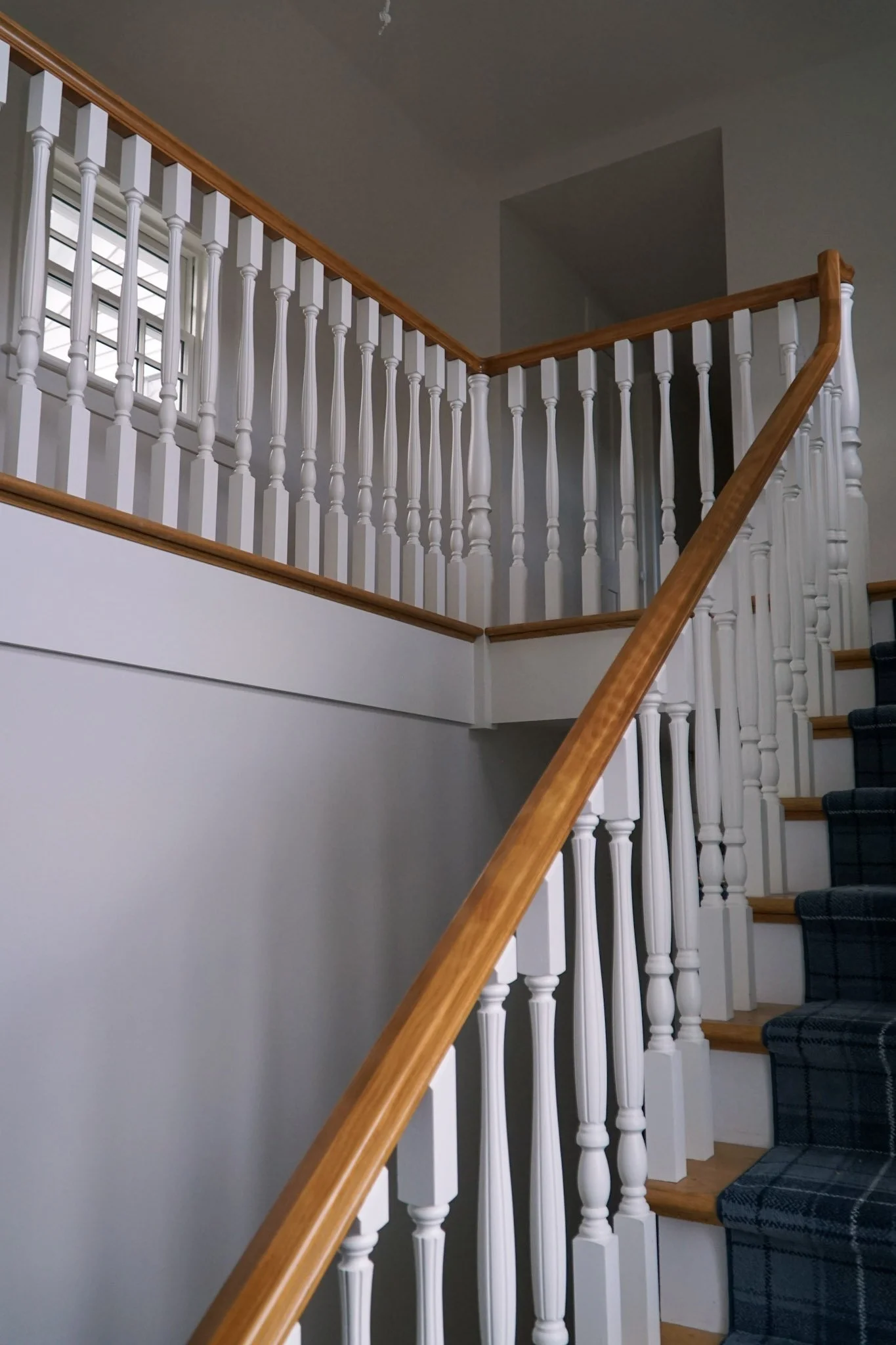 Stair railings with a wooden top and white pillars for the base. They follow the stairs up and then around the open balcony at the top. 