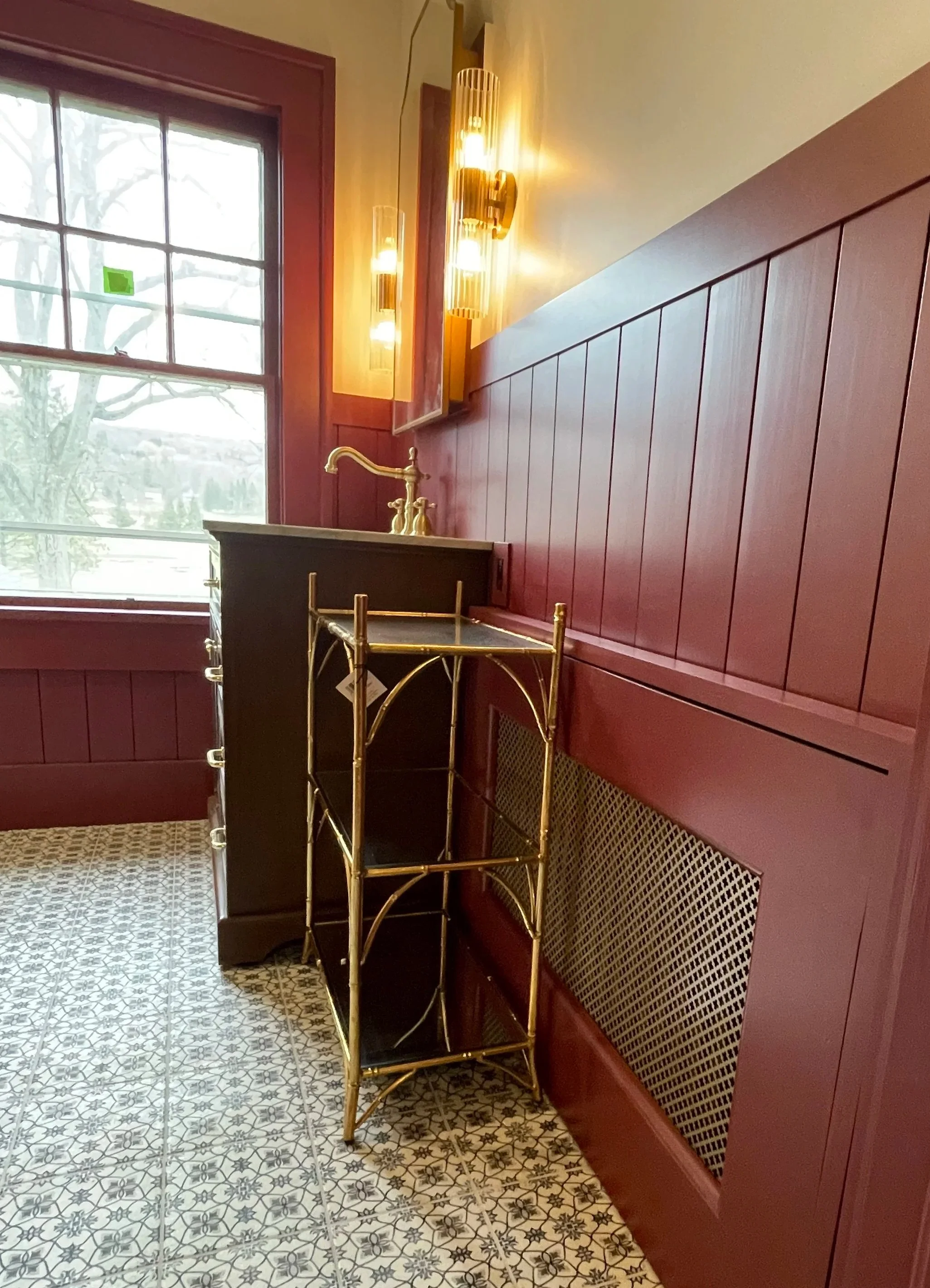 Interior of a room with a large window, red-paneled walls, a gold and black cart, and gold light fixtures on the wall.