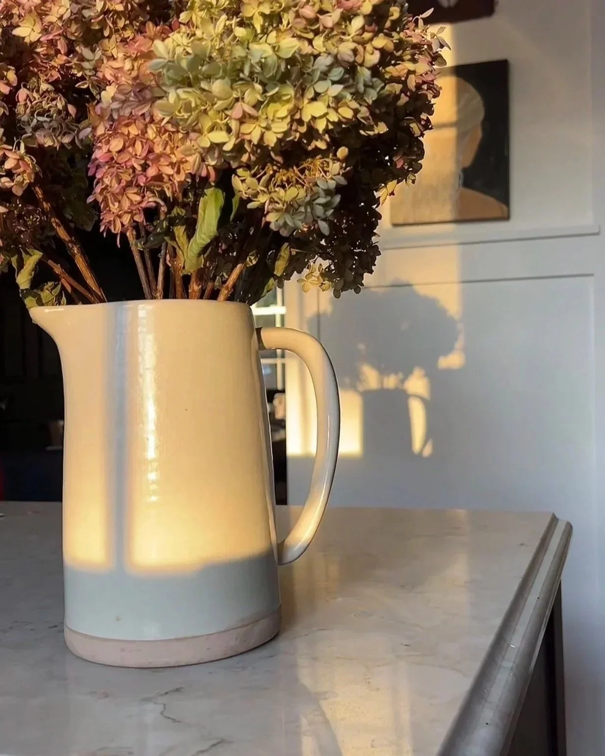 A pitcher of flowers sits on a quartz countertop on a custom island. Wainscoting millwork is in the background. From a historic home in central new york.
