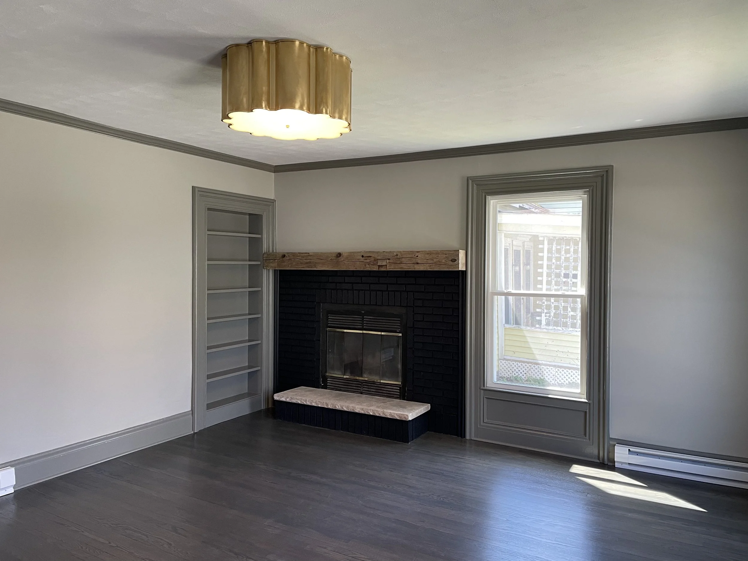 Empty living room with a fireplace, built-in shelves, a window, modern light fixture, and hardwood flooring.