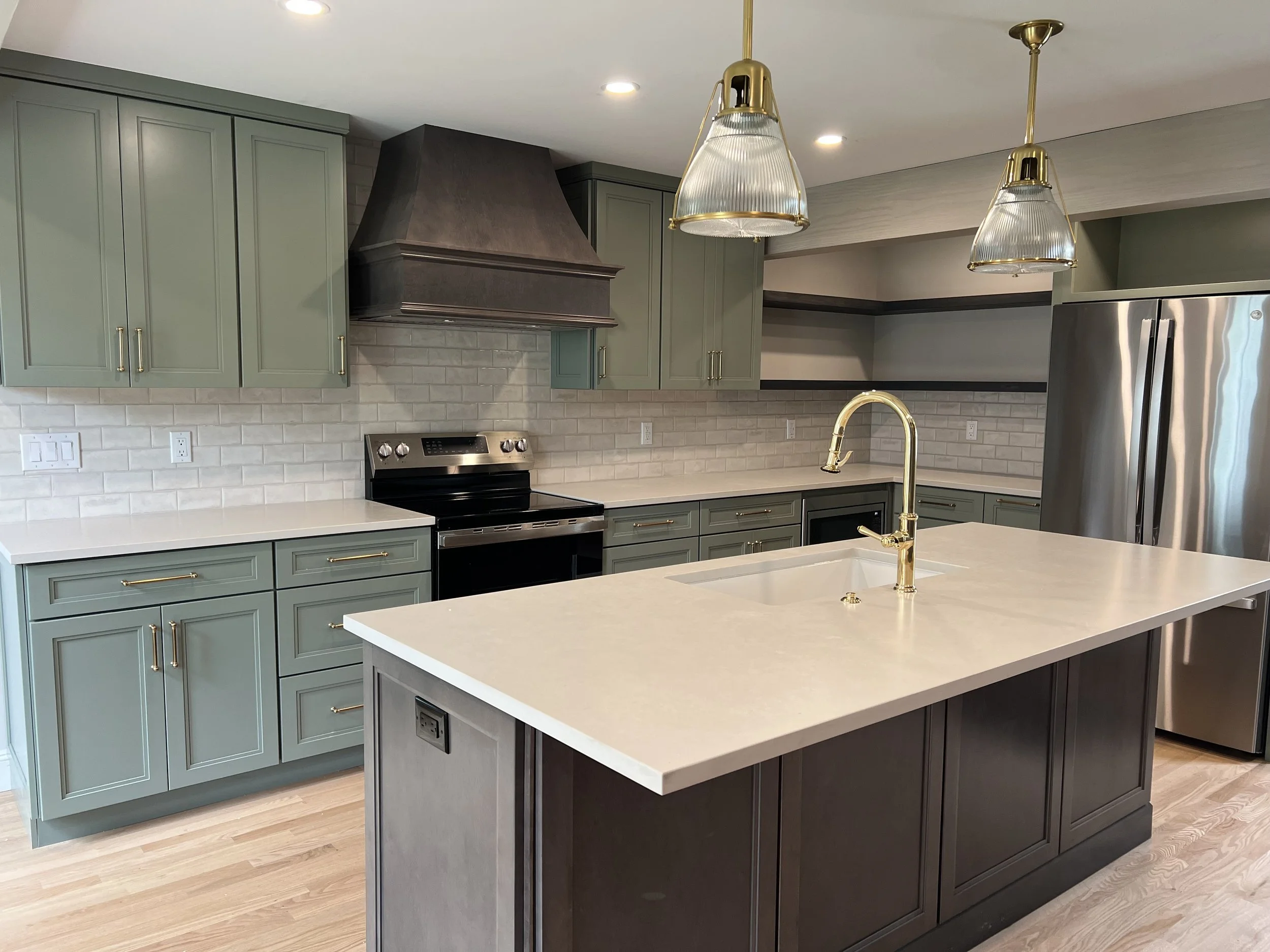 A new kitchen remodel with sage green cabinets, a maple stained island, brass pendant lights and an unlaquered brass faucet completed by a construction company in Hamilton, NY.