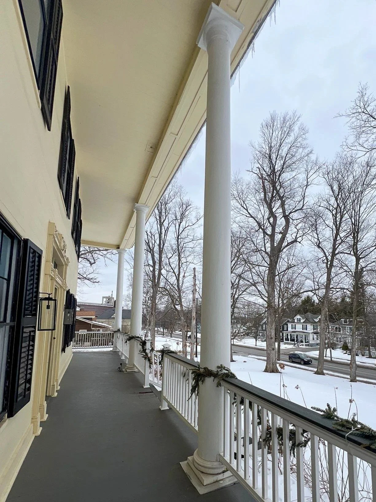 Historic solid timber columns on a home in New Hartford New York. The house is yellow with black shutters and the front porch is painted gray. Columns in various states of decay are present.