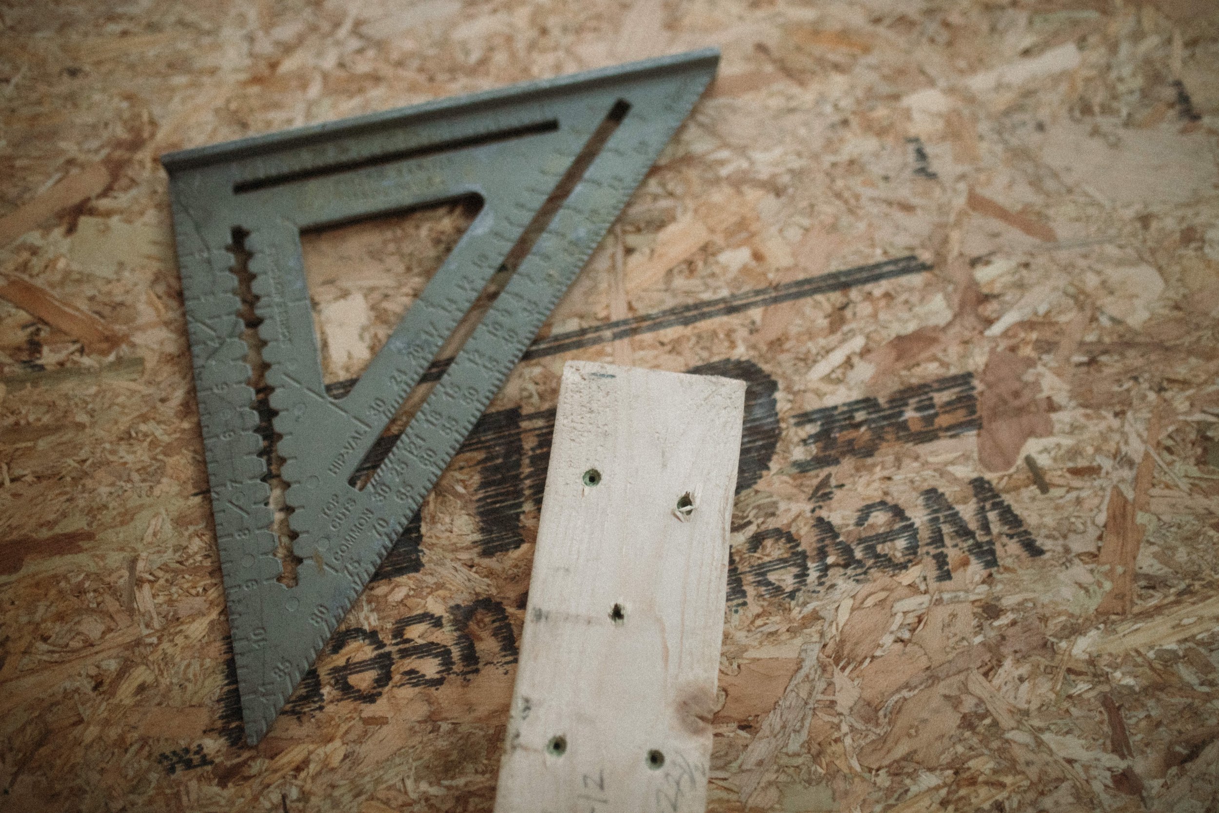 A measuring triangle tool and a board with nails in it lies on plywood.