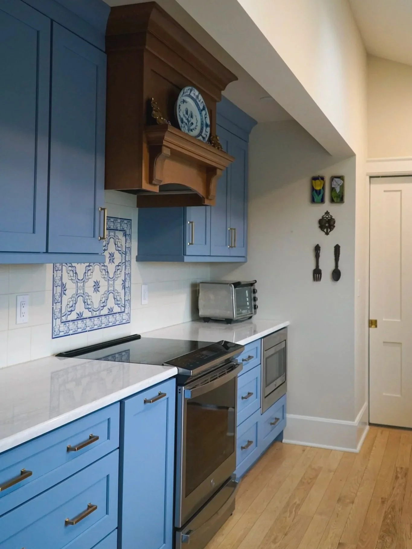 A newly remodeled kitchen with blue cabinets and a stained wood range hood and custom tile detail was part of a renovation in Central New York.