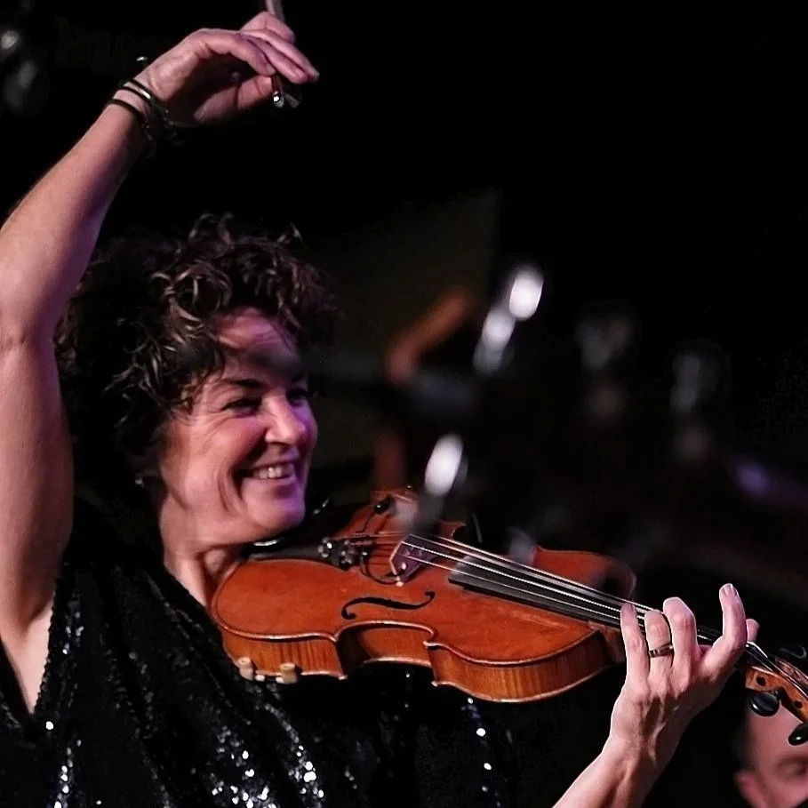 Een vrouw met krullend bruin haar speelt viool.