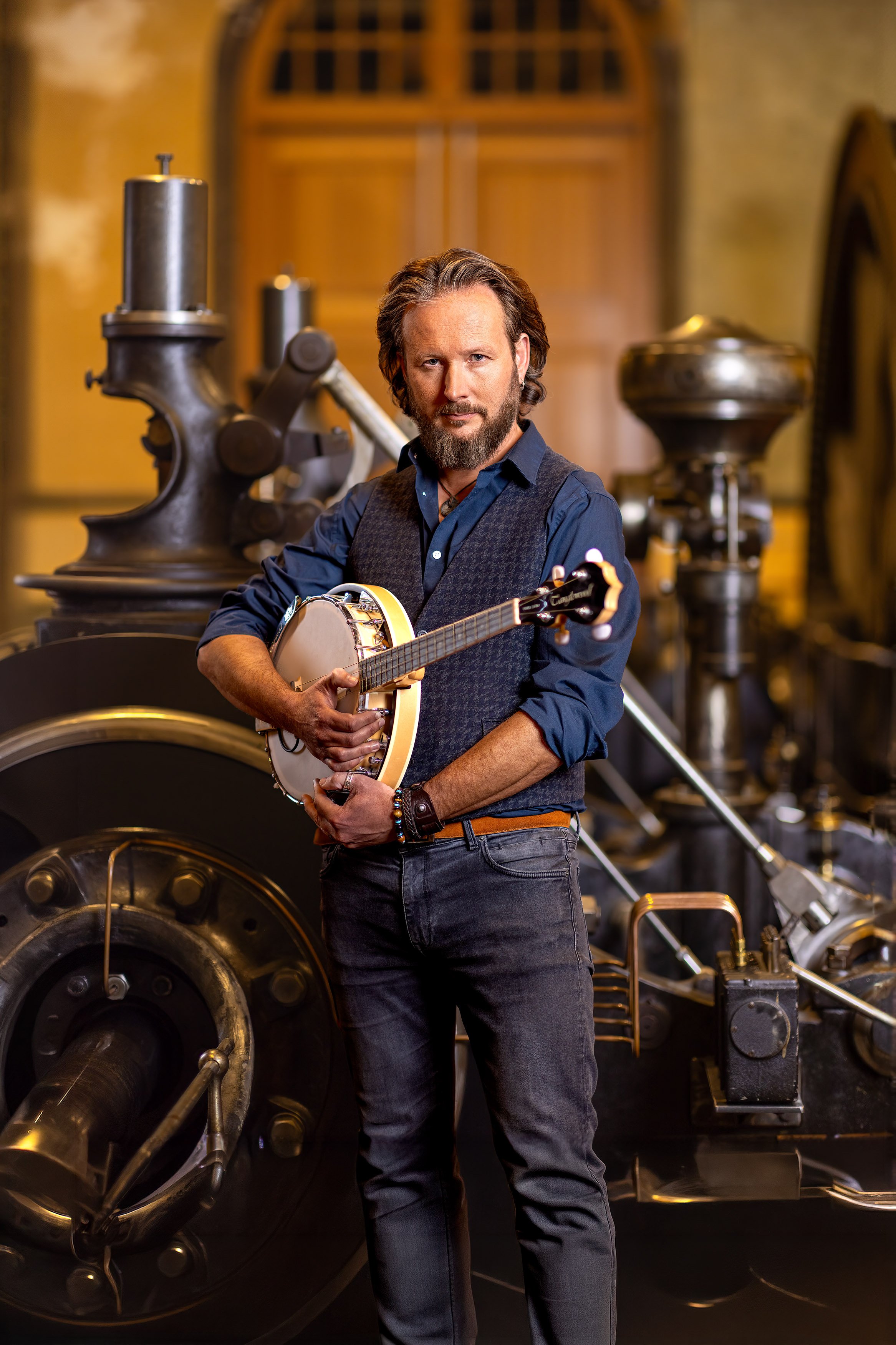 Man met een baard en lang haar houdt een gitaar vast dicht bij zijn gezicht, met een bakstenen muur op de achtergrond.