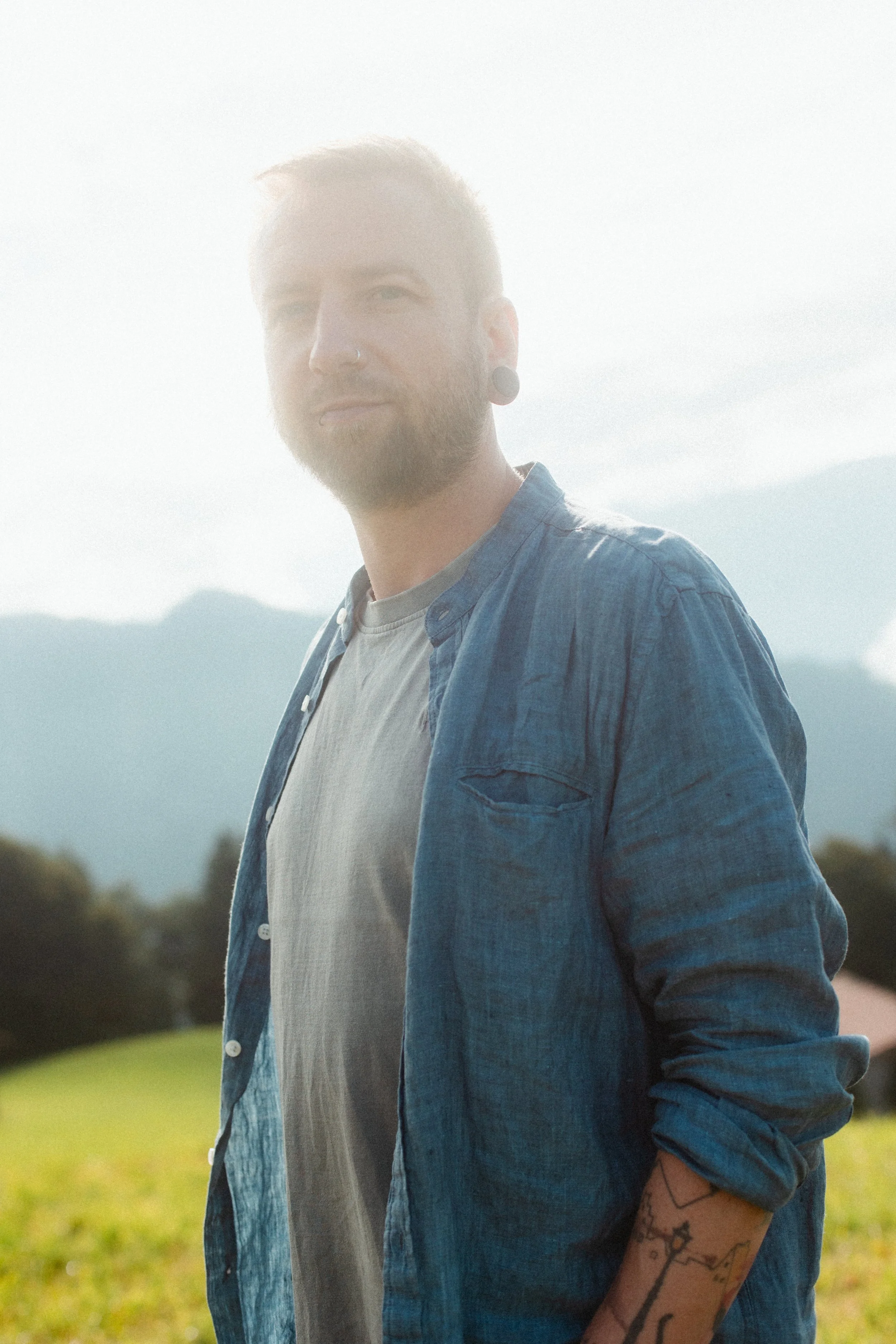 Richard Milde, Life Coach aus Interlaken, lächelnd auf einer grünen Wiese vor verschwommenem Bergpanorama im warmen Gegenlicht