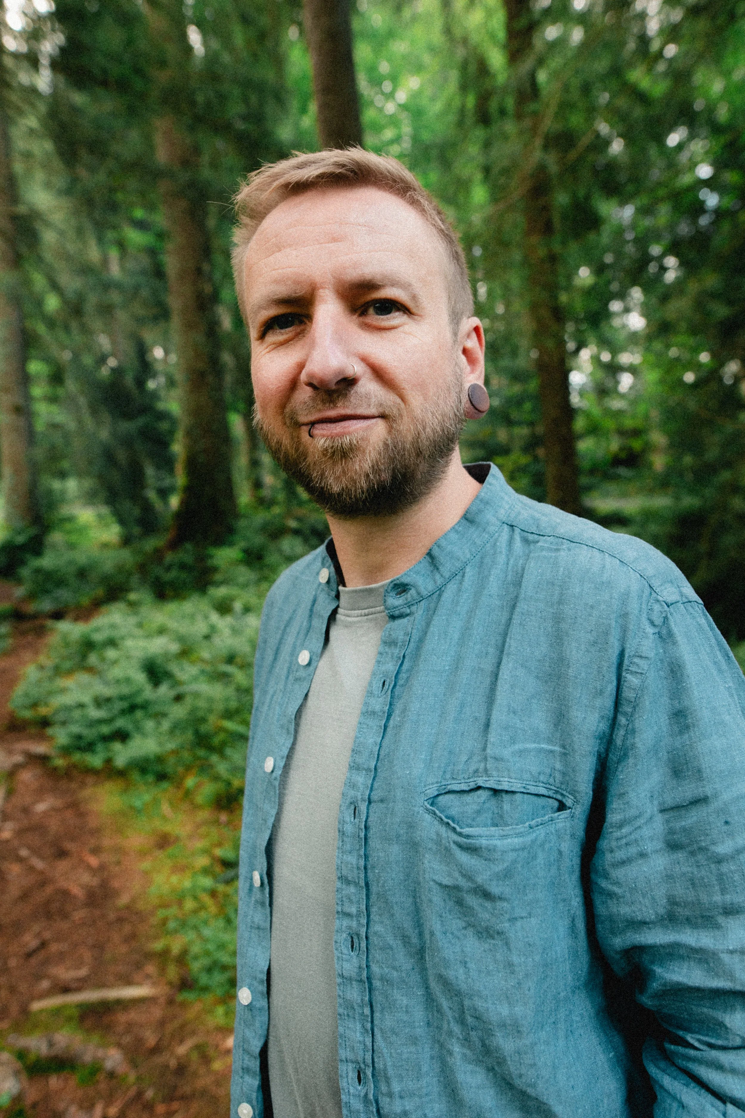 Richard Milde, Life Coach aus Interlaken, lächelnd im Wald mit unscharfem Baum- und Blätterhintergrund