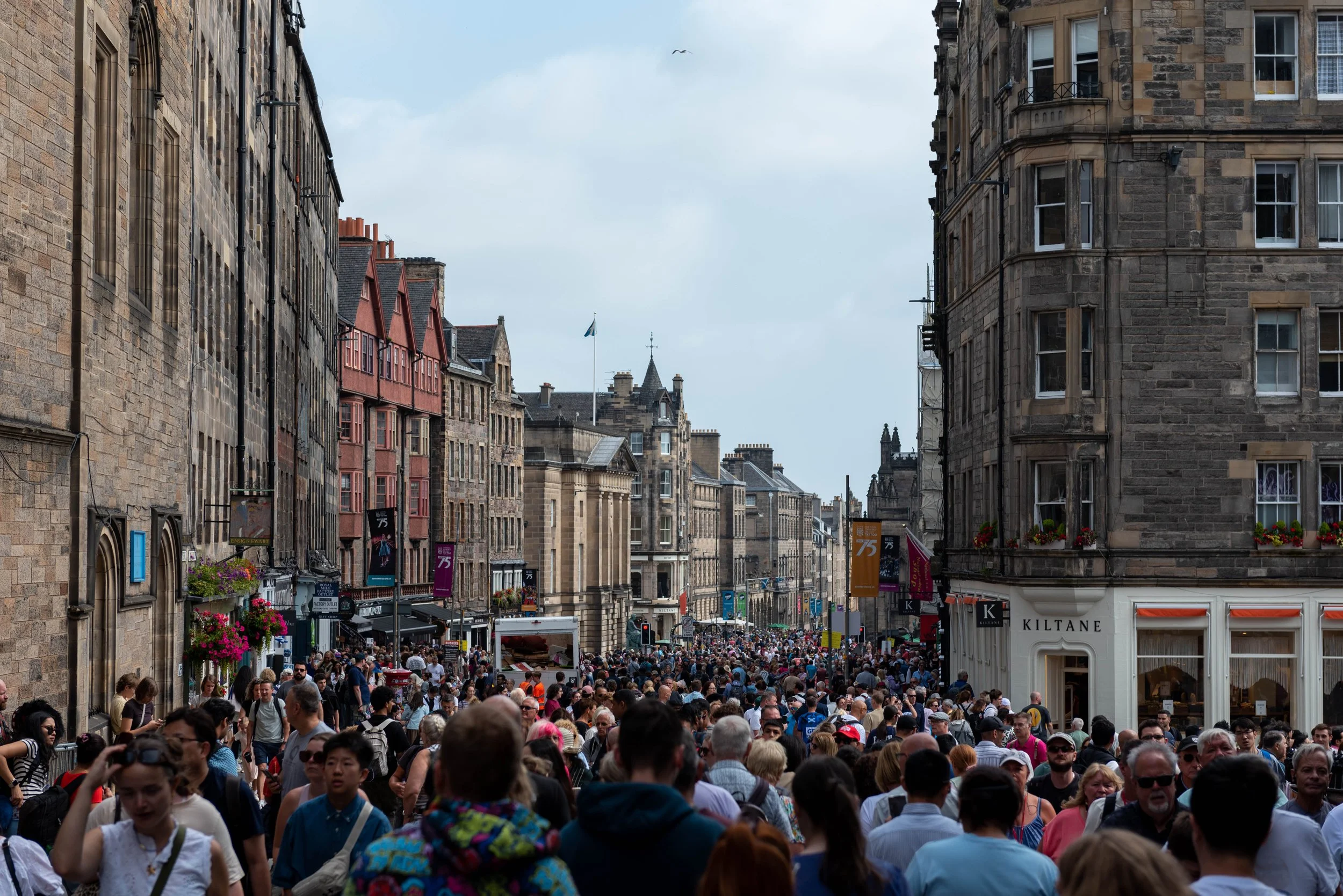 Crowds of people walking along the Royal Mile in Edinburgh during festival season, with historic buildings lining the street
