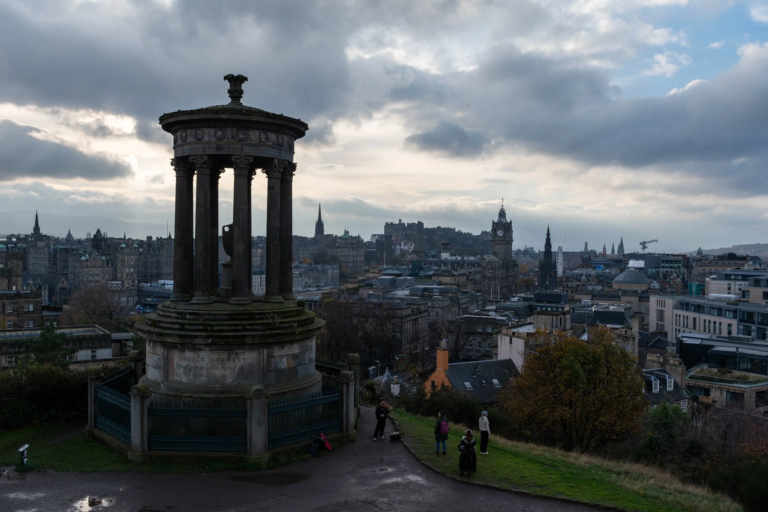 View from Calton Hill overlooking Edinburgh’s skyline on a cloudy, atmospheric day, with historic monuments in the foreground