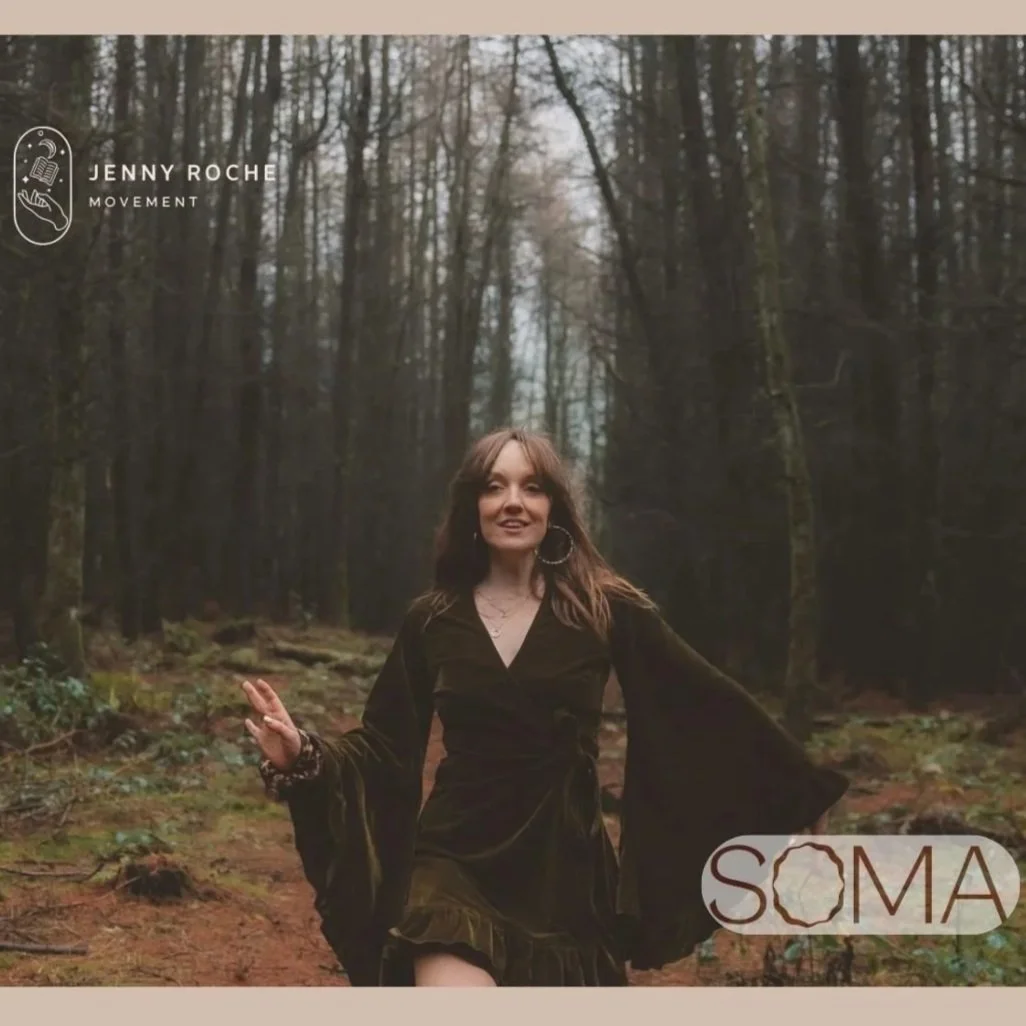 A young woman with long brown hair wearing a dark dress with flared sleeves, walking through a forested area with tall trees and green foliage. She is smiling and gesturing with her left hand. The image includes text overlay with the name Jenny Roche and the words 'Movement' and 'SOMA'.