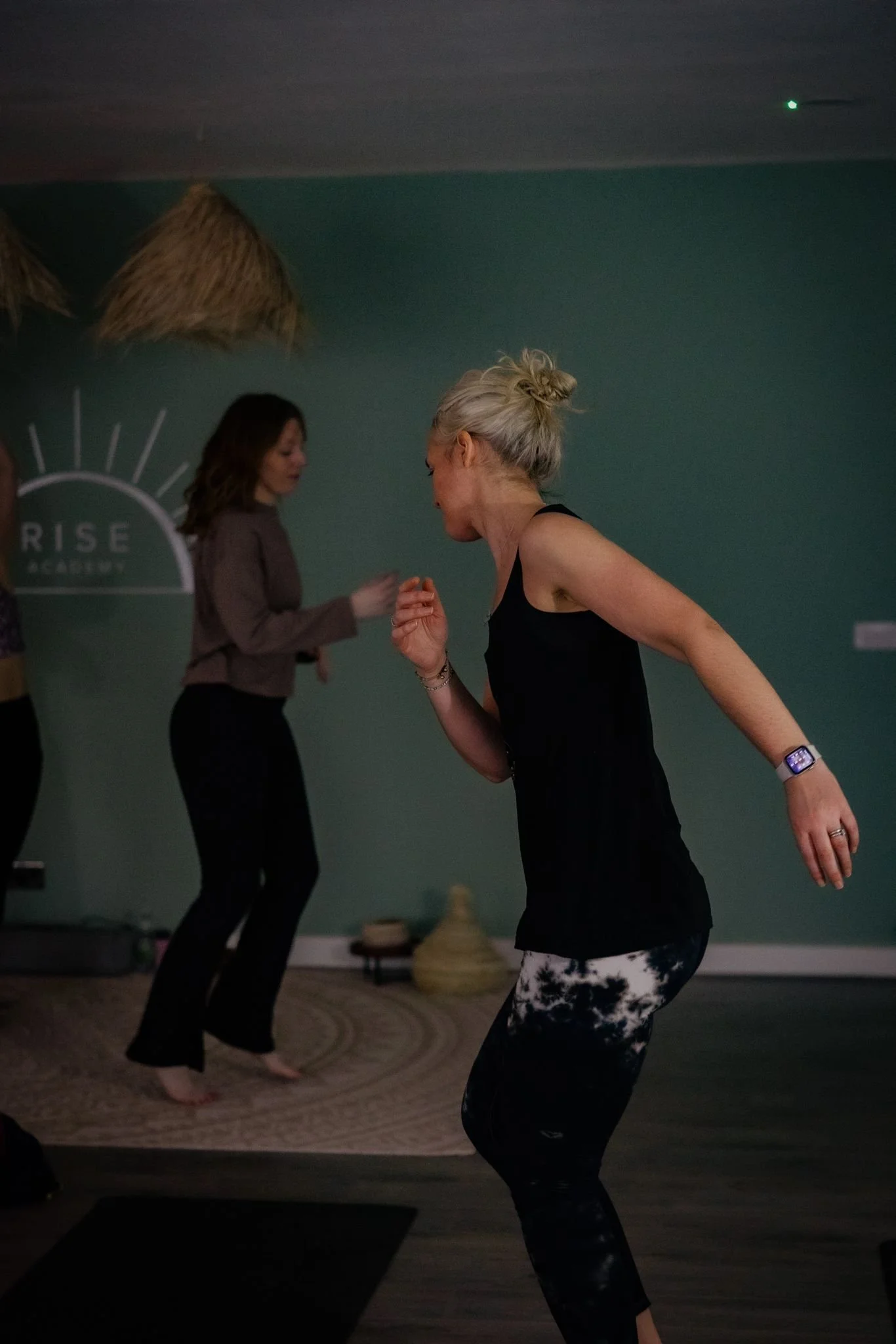 Women practicing dance or yoga in a studio with green walls and beach-themed decor.