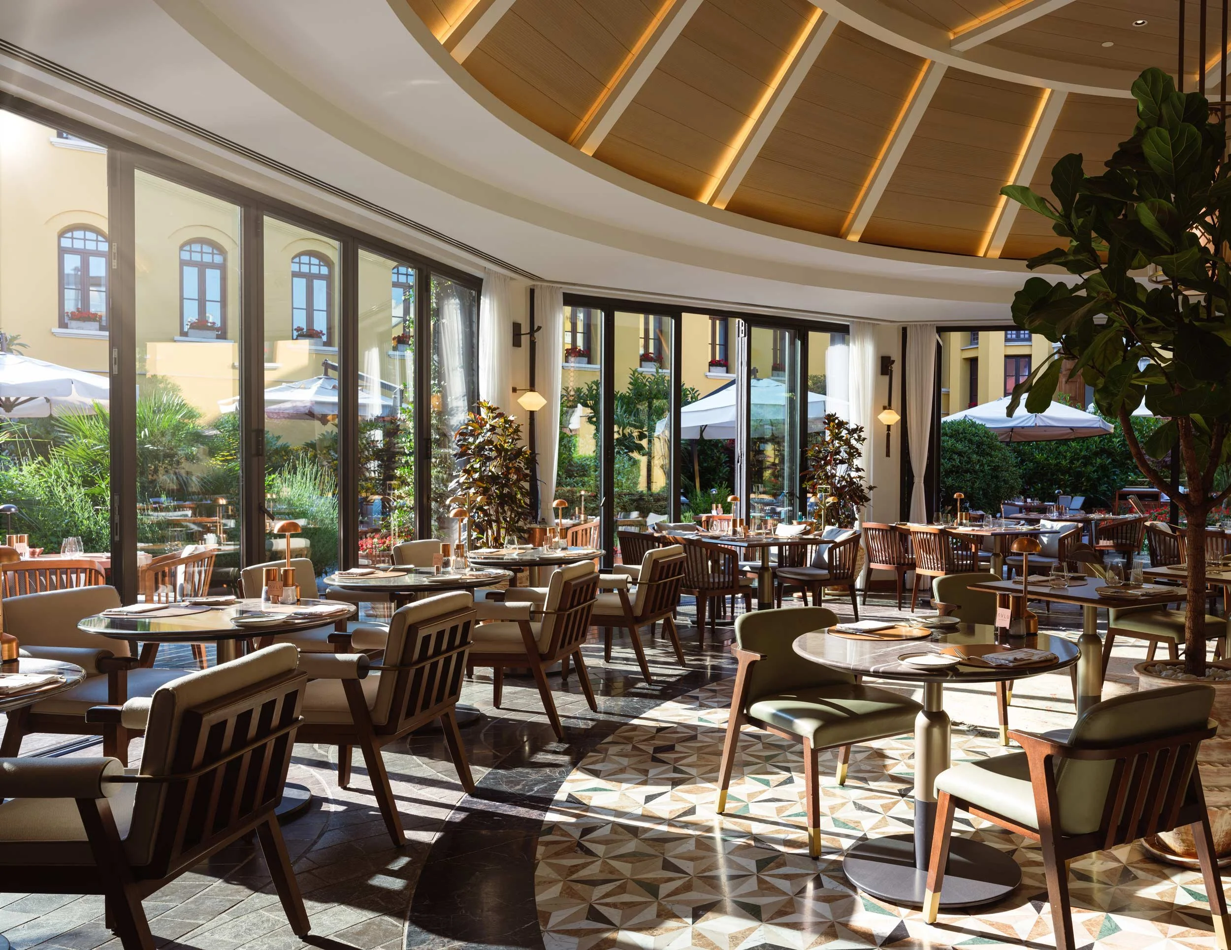 Upscale restaurant with large glass windows, stylish tables and chairs, natural sunlight, and outdoor patio area visible through the windows at Four Seasons Istanbul Hotel at Sultanahmet.