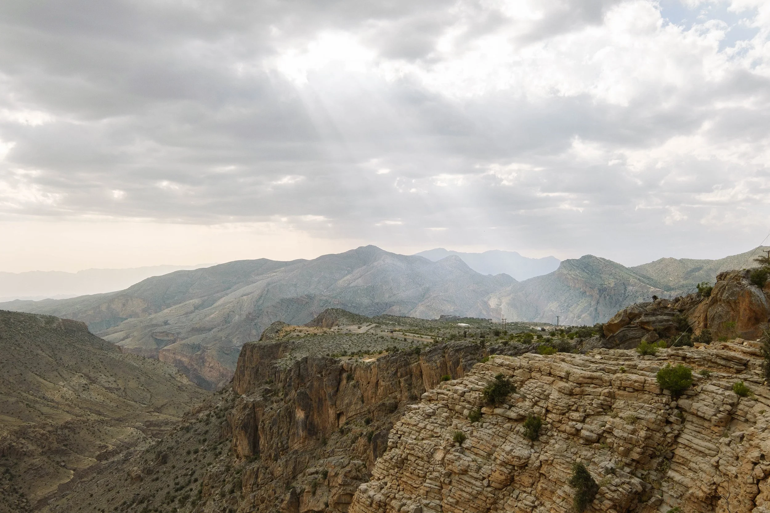 Mountain landscape with layered rock formations, distant mountains, and a cloudy sky