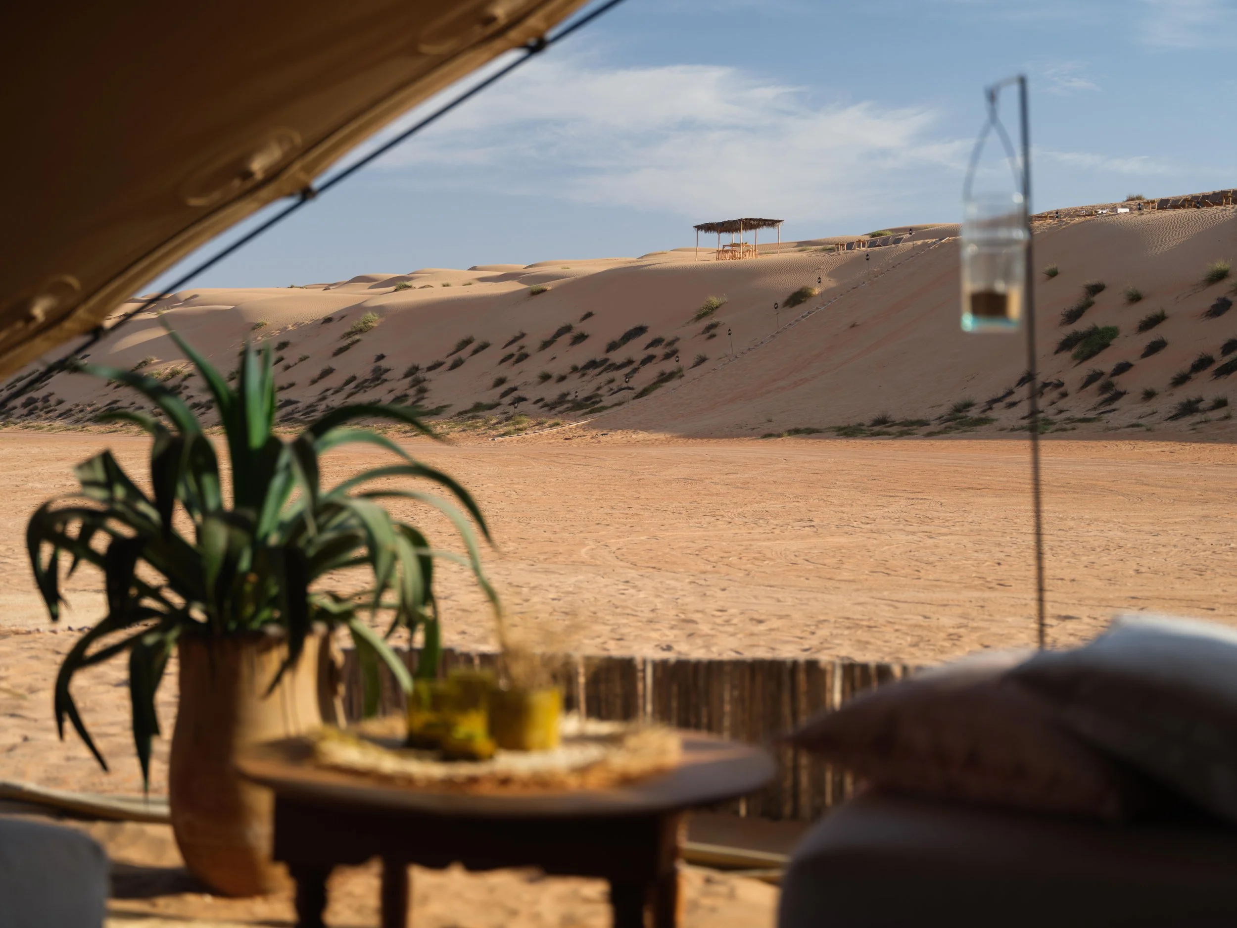 Desert landscape with sand dunes, potted plant, and outdoor seating area under a canopy tent.